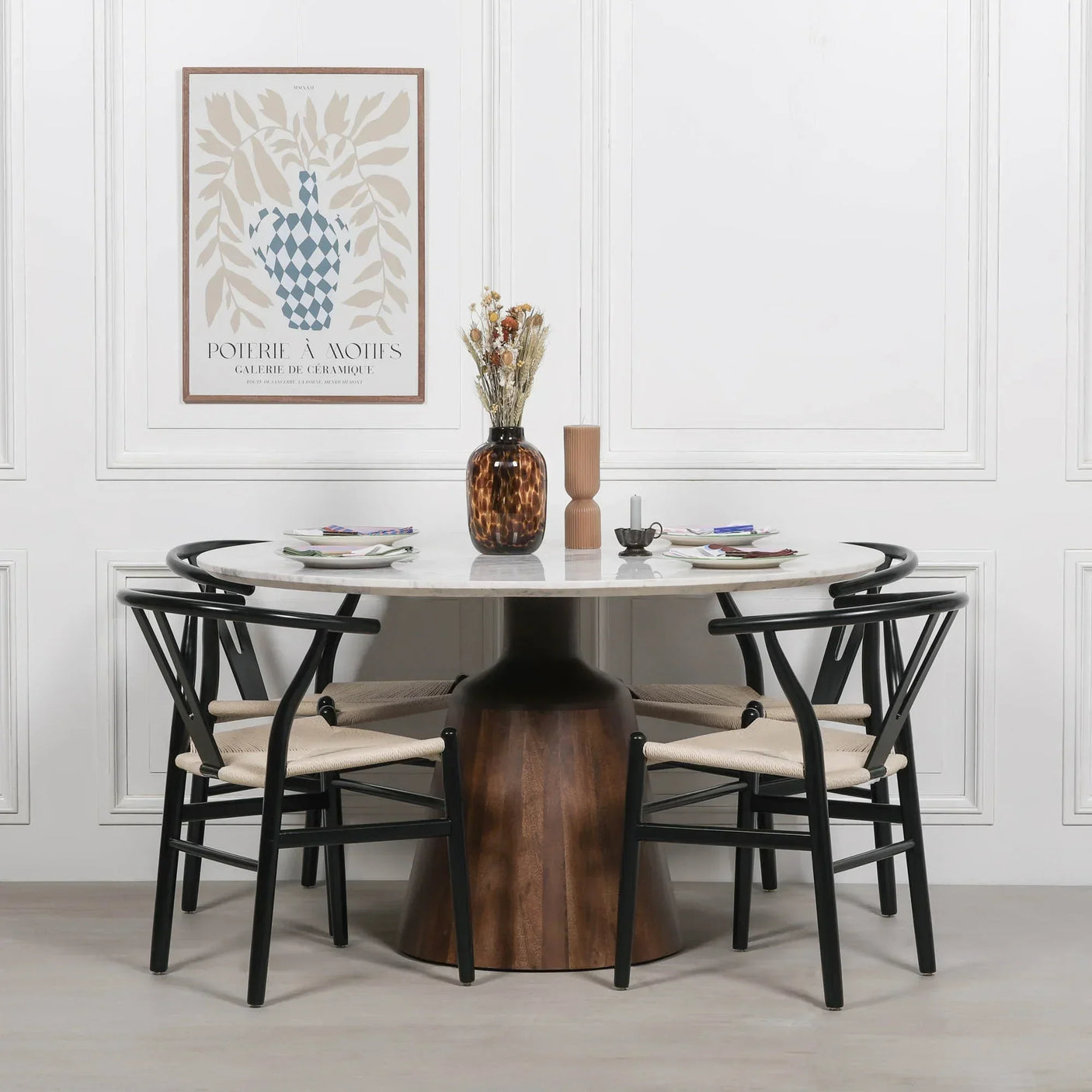 Round marble dining table with wood pedestal base and four black dining chairs in modern room