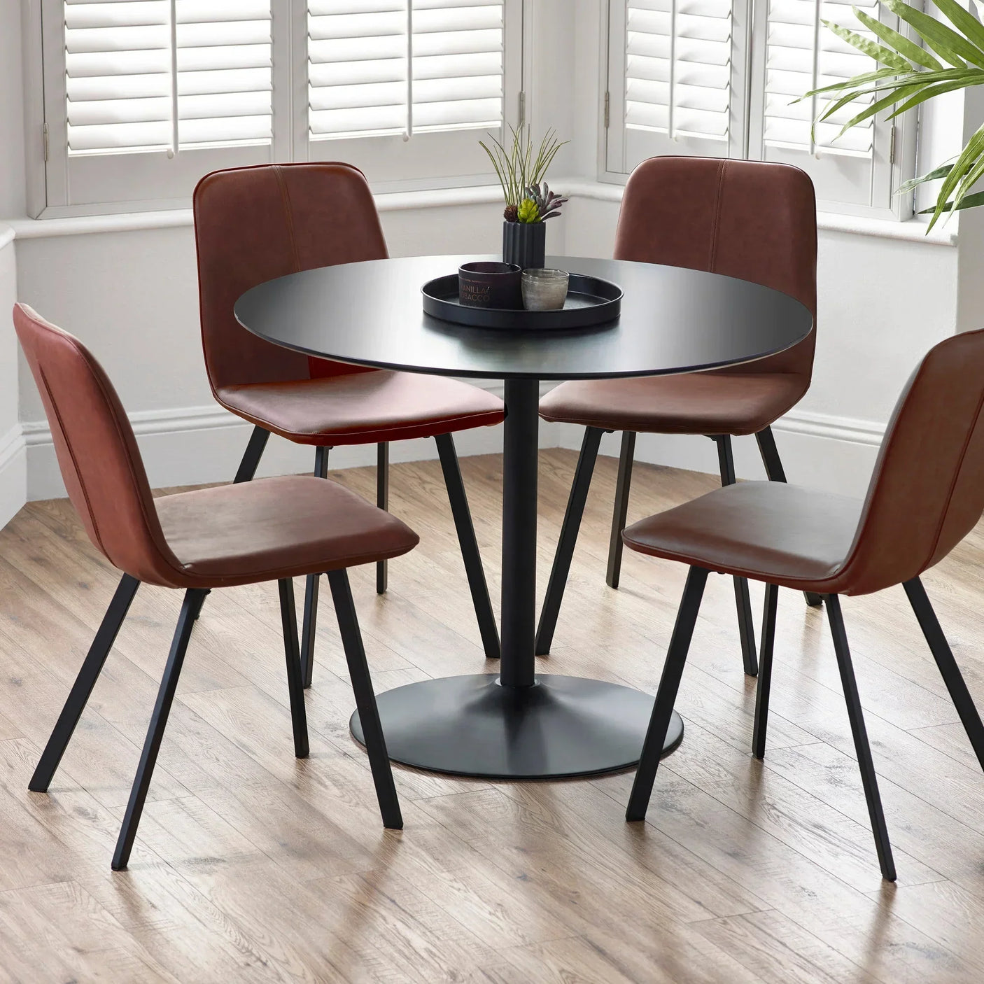 Round black dining table with four brown faux leather chairs on wood floor