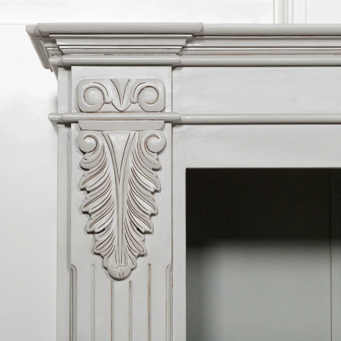 Grey painted fireplace with decorative carved wood detailing and classical scroll design