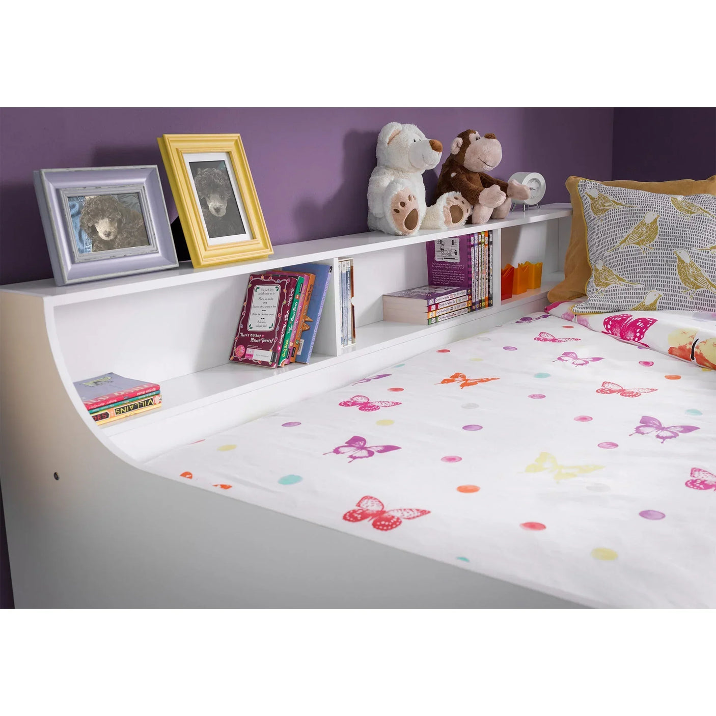 White daybed with bookshelf headboard, children's bedding, toys, books, and picture frames