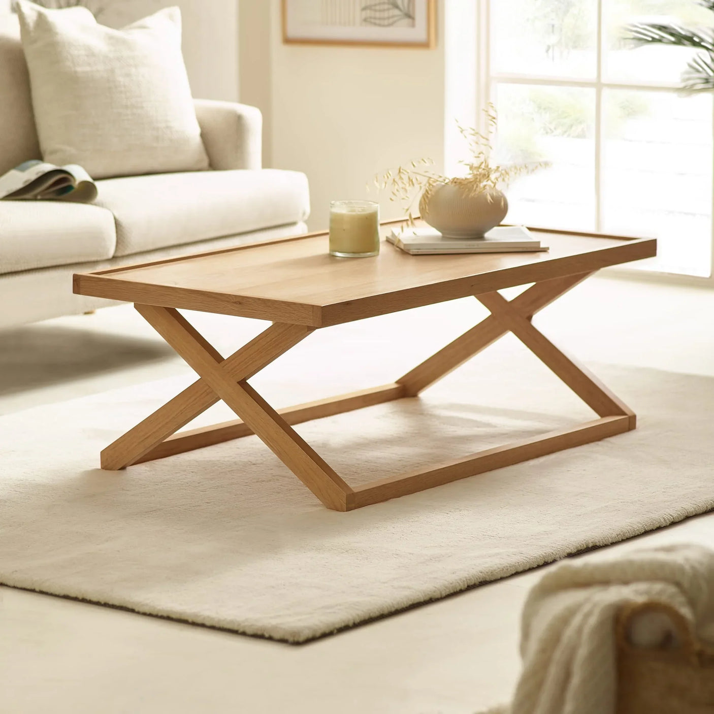 Wooden coffee table with X-frame legs on cream rug in bright living room