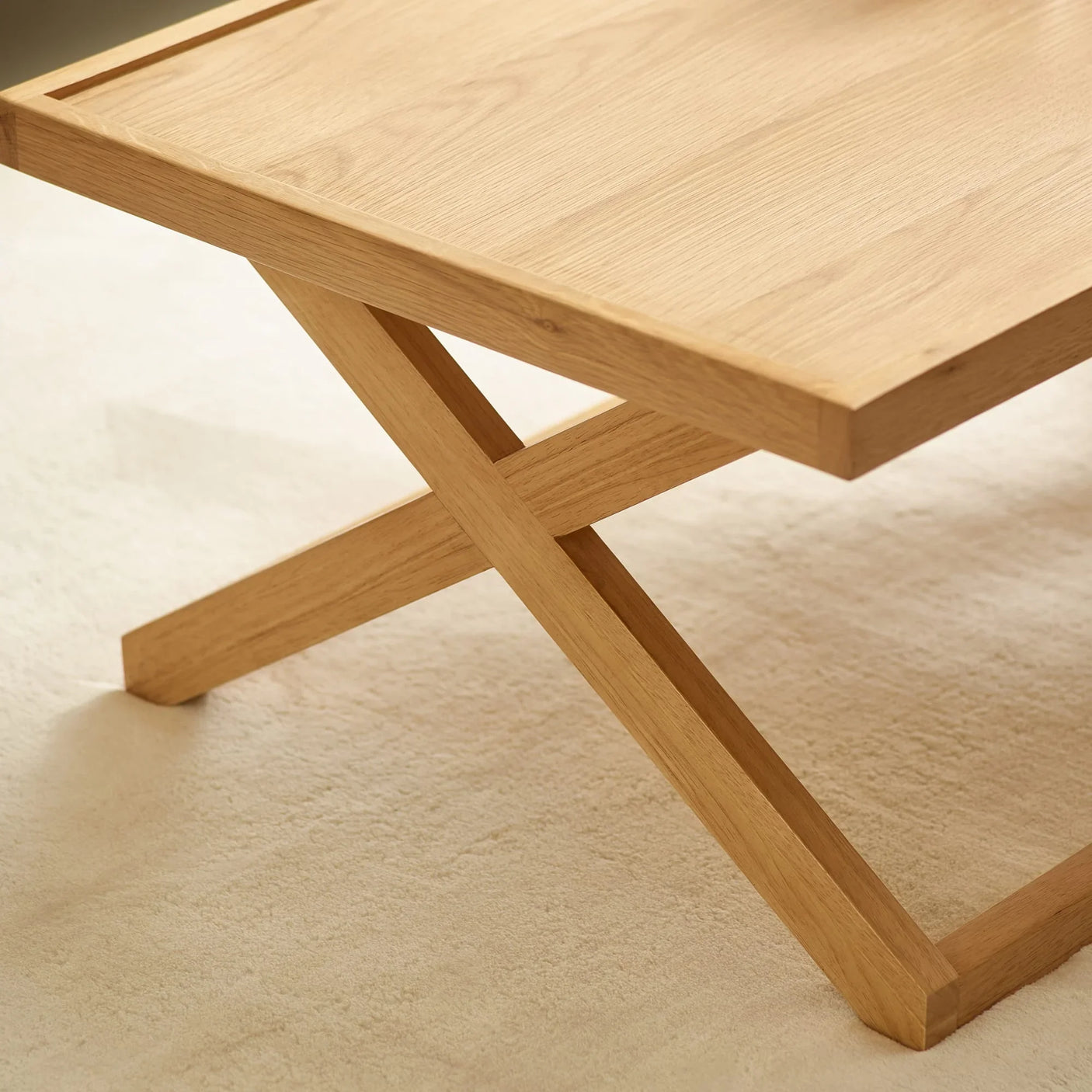 Oak coffee table with angled cross legs on light carpet