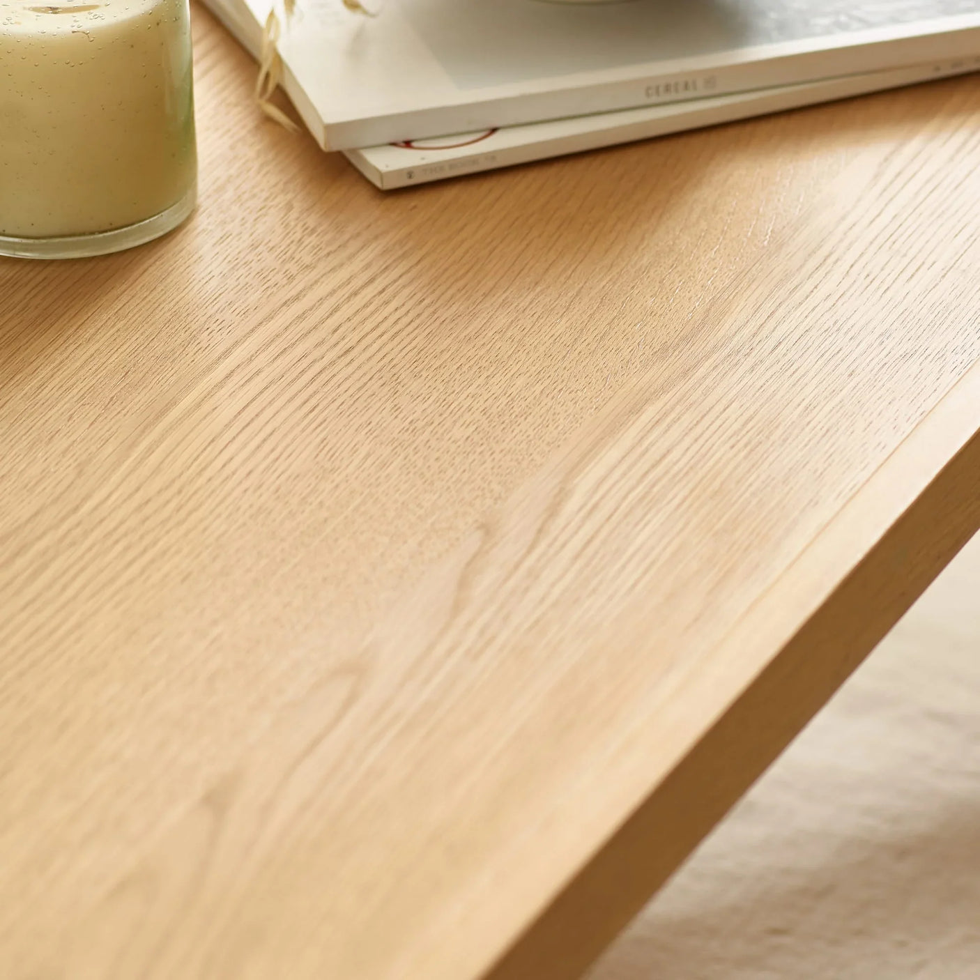 Close up of light oak dining table surface with candle and stacked magazines
