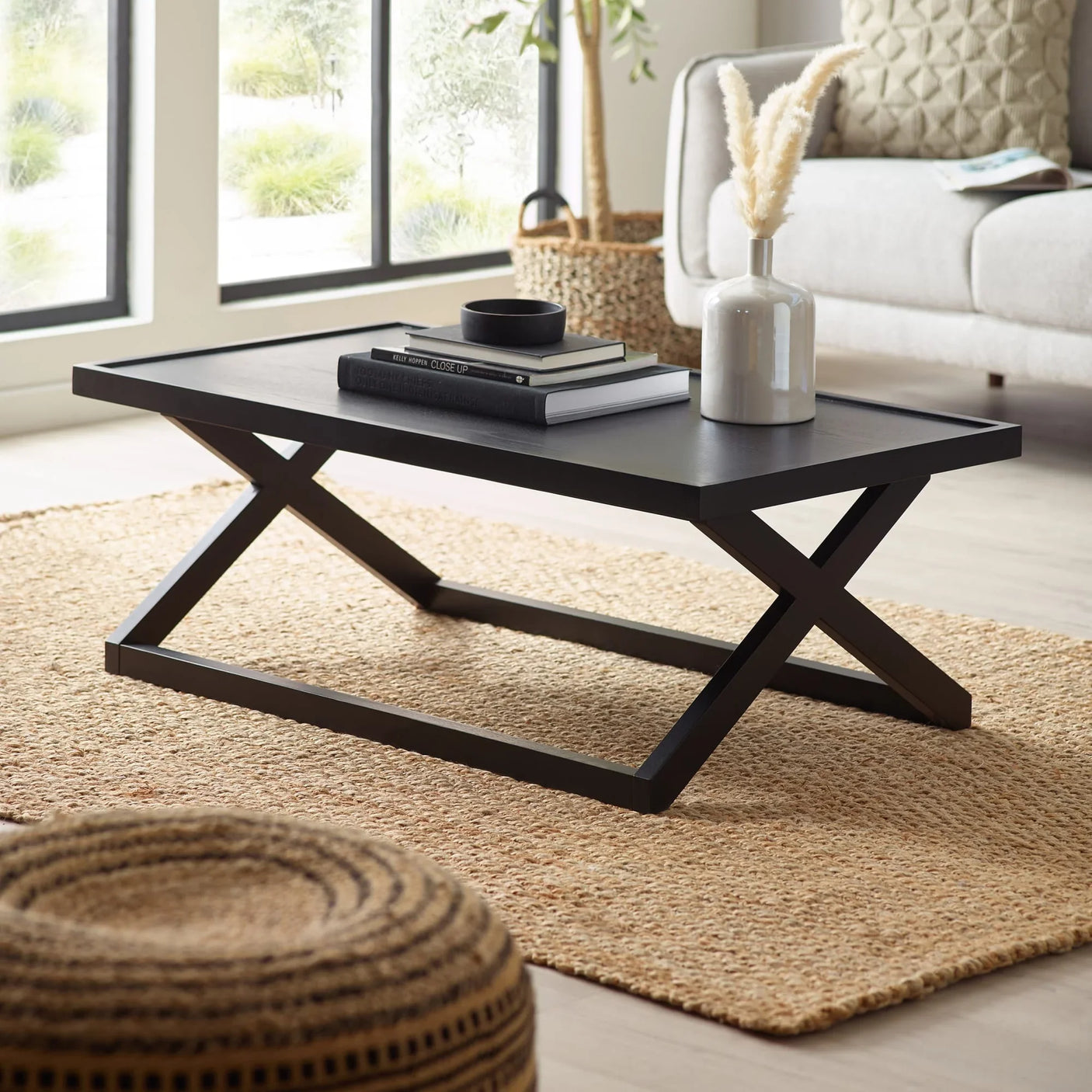 Black wooden coffee table with crossed legs on jute rug in modern living room setting