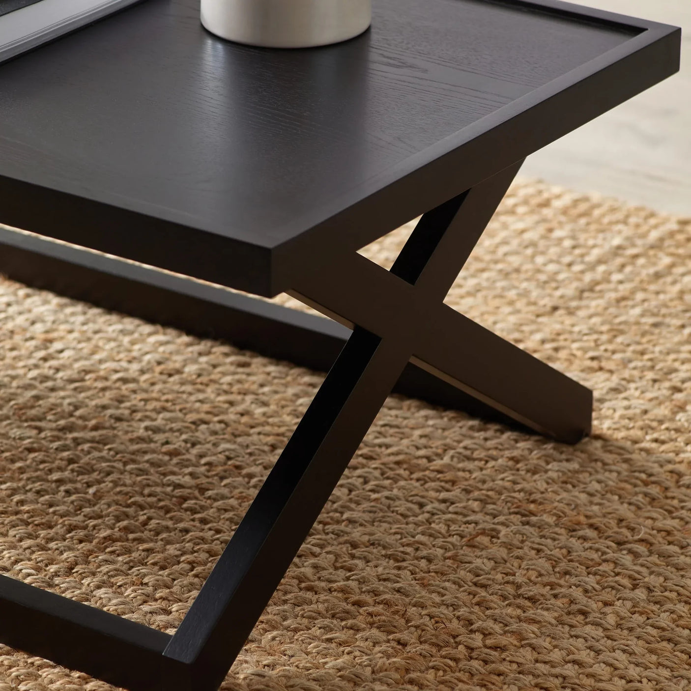 Black wooden coffee table with X-frame legs on woven jute rug