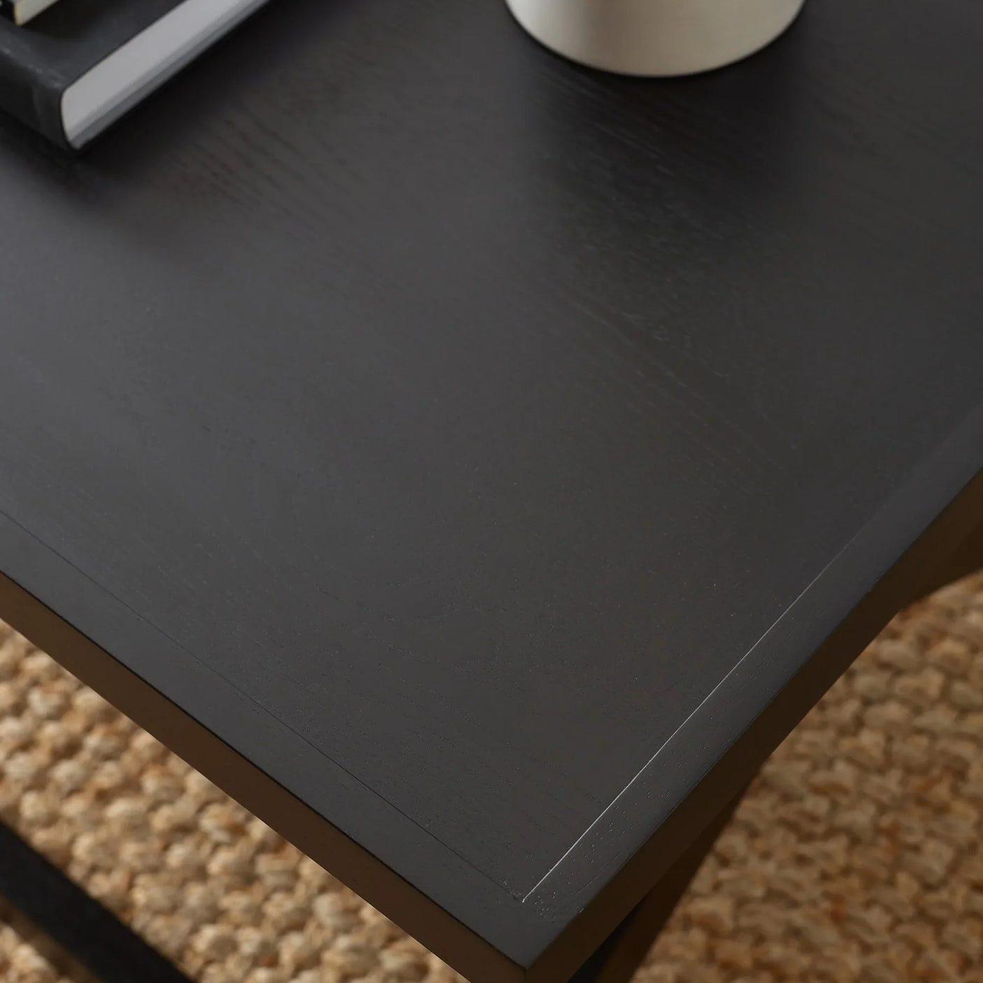 Black wood coffee table corner with smooth finish next to woven rug