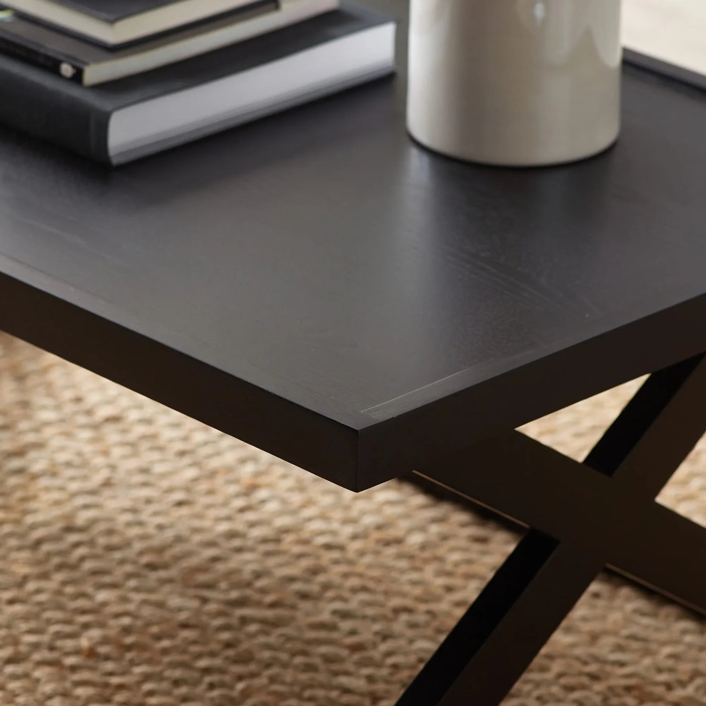 Black coffee table with cross metal legs, close view showing textured wood surface and decor items