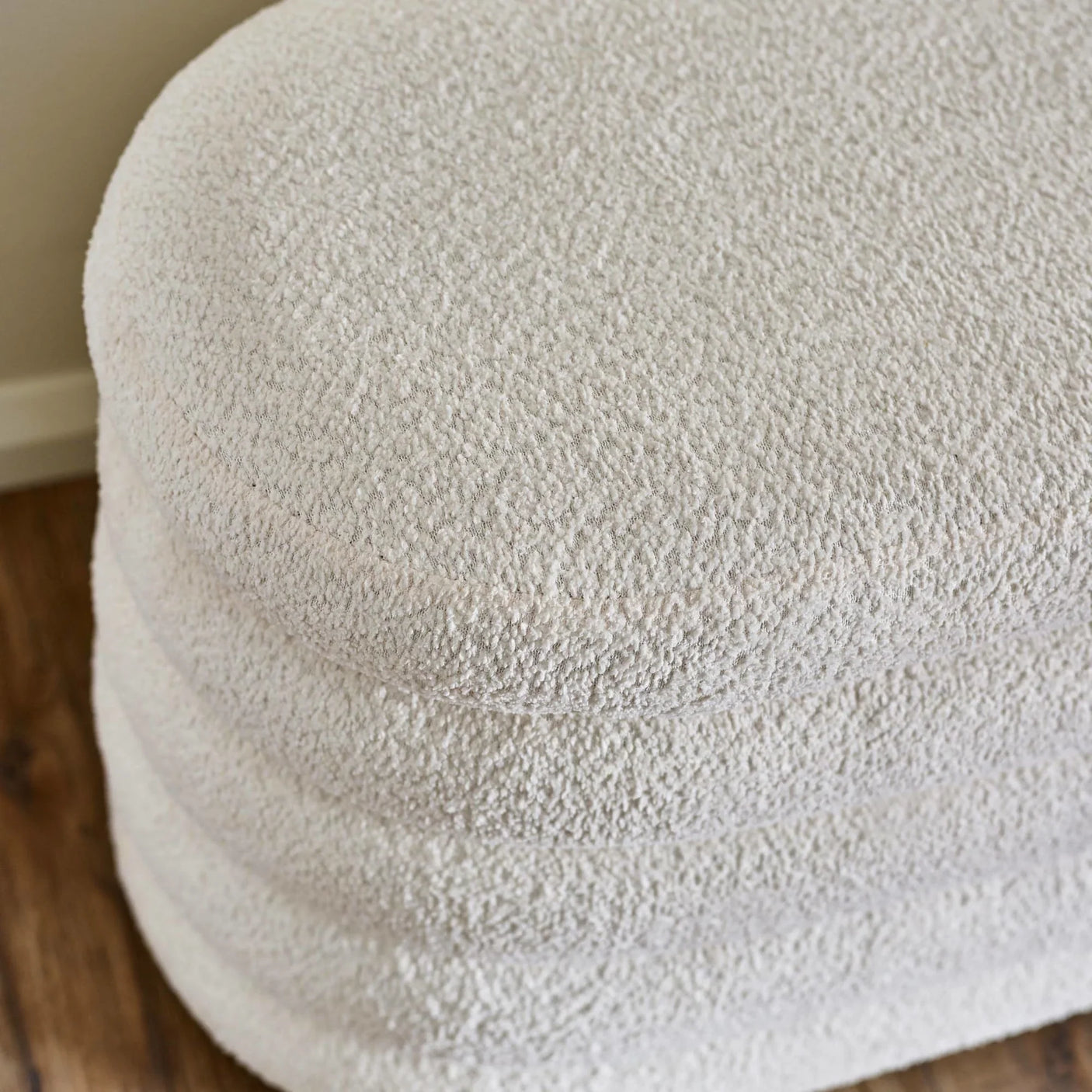 Cream boucle upholstered ottoman with textured fabric, close-up of rounded top