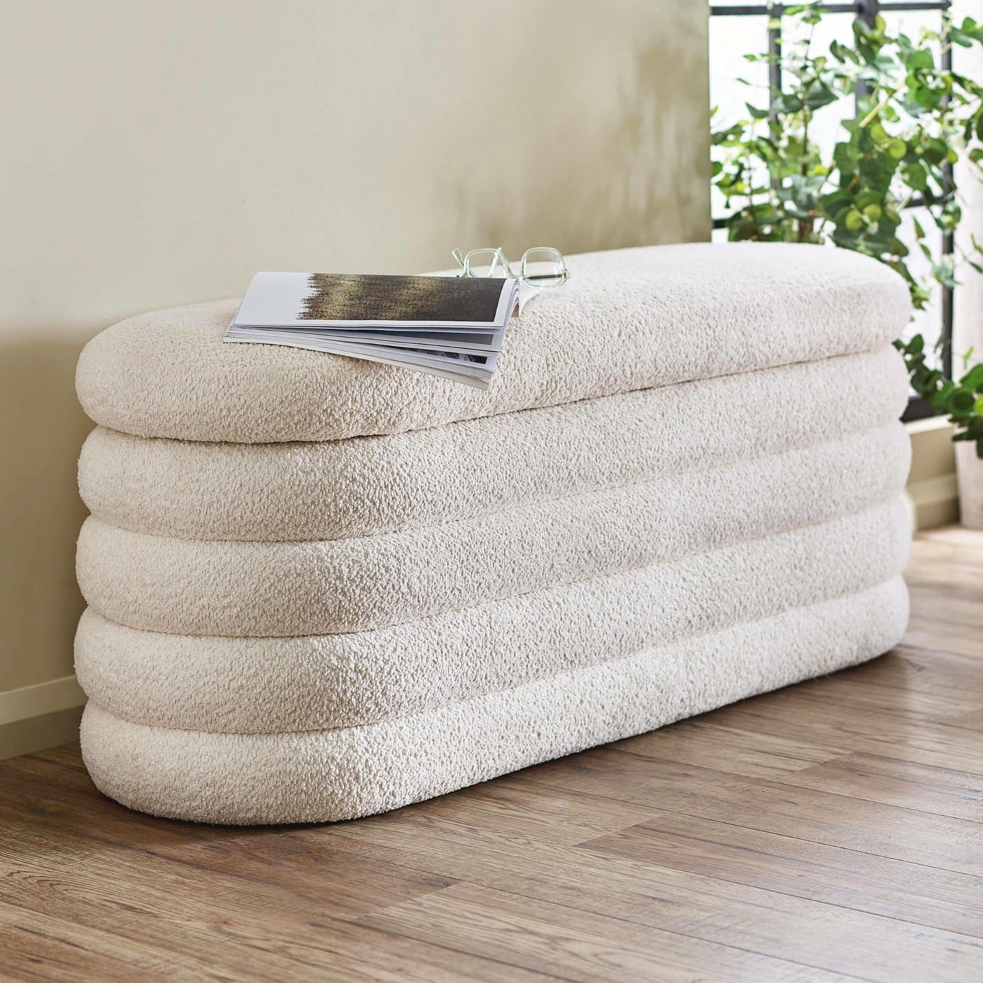 Cream boucle bench seat with stacked design on wooden floor beside window and indoor plant