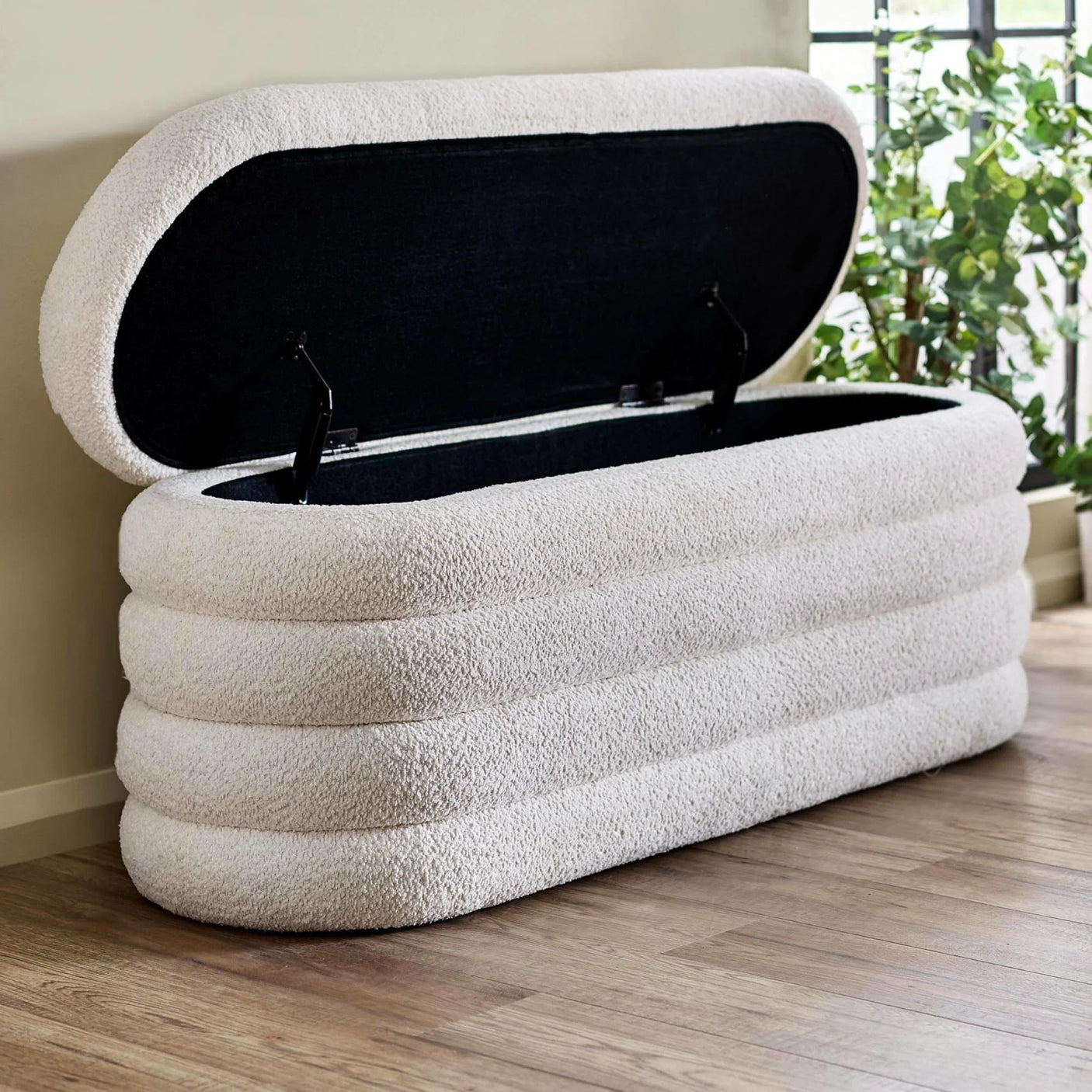 Cream bouclé storage bench with open lid on wood floor near window