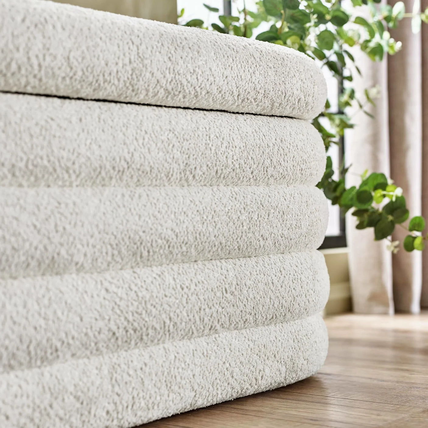 Stack of cream bath towels with textured fabric near window and green plant