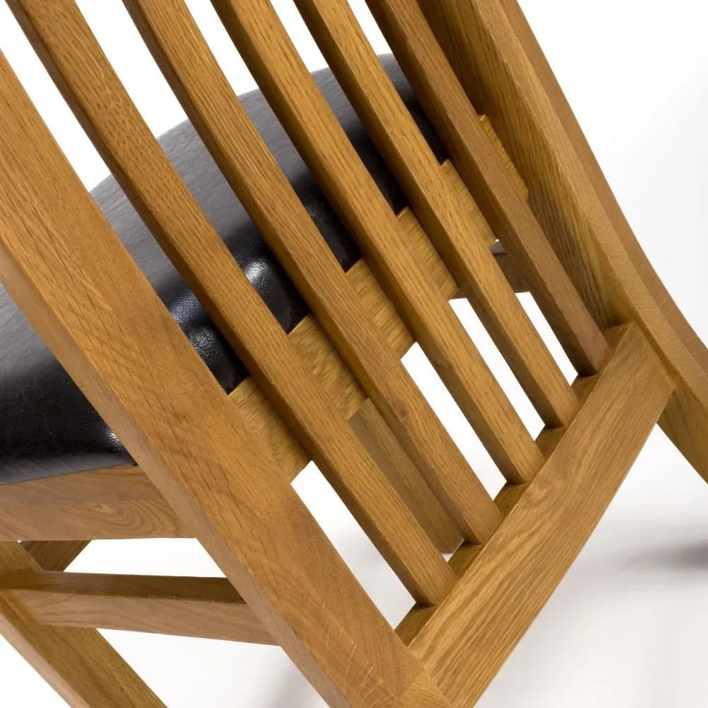 Oak dining chair with vertical slat back and black padded seat, close-up angle