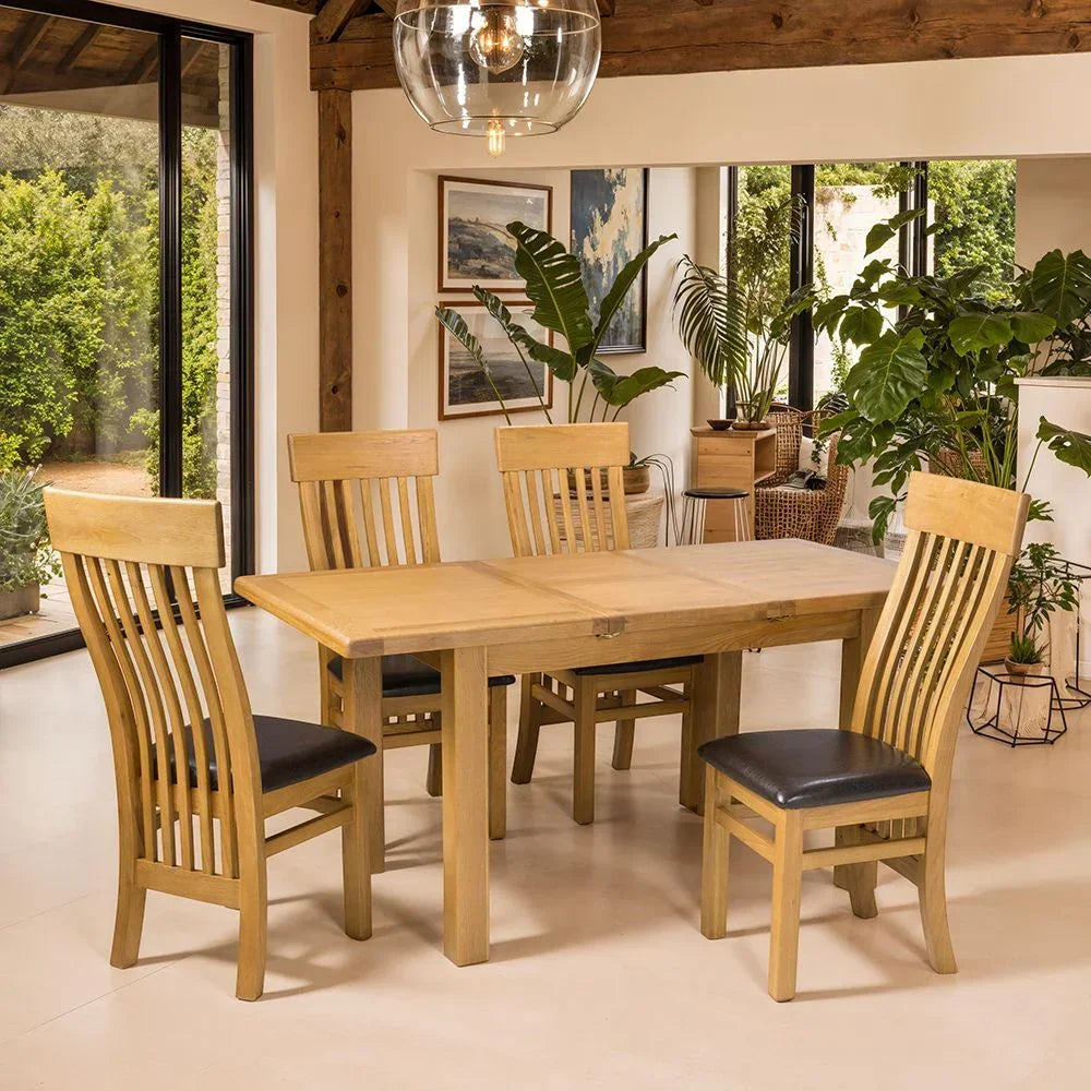 Solid oak dining table with four slat-back chairs and black seat pads in a bright room
