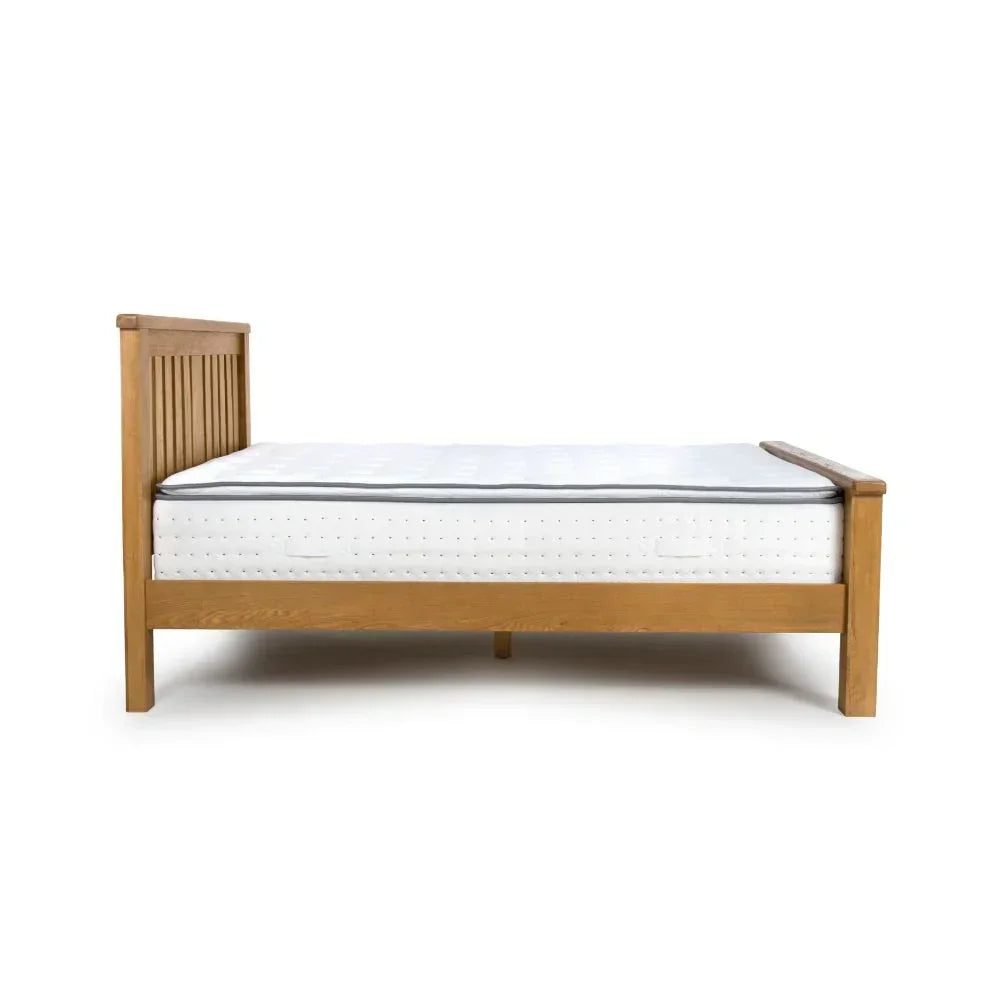 Oak wooden bed frame with vertical slat headboard and white mattress, side profile view