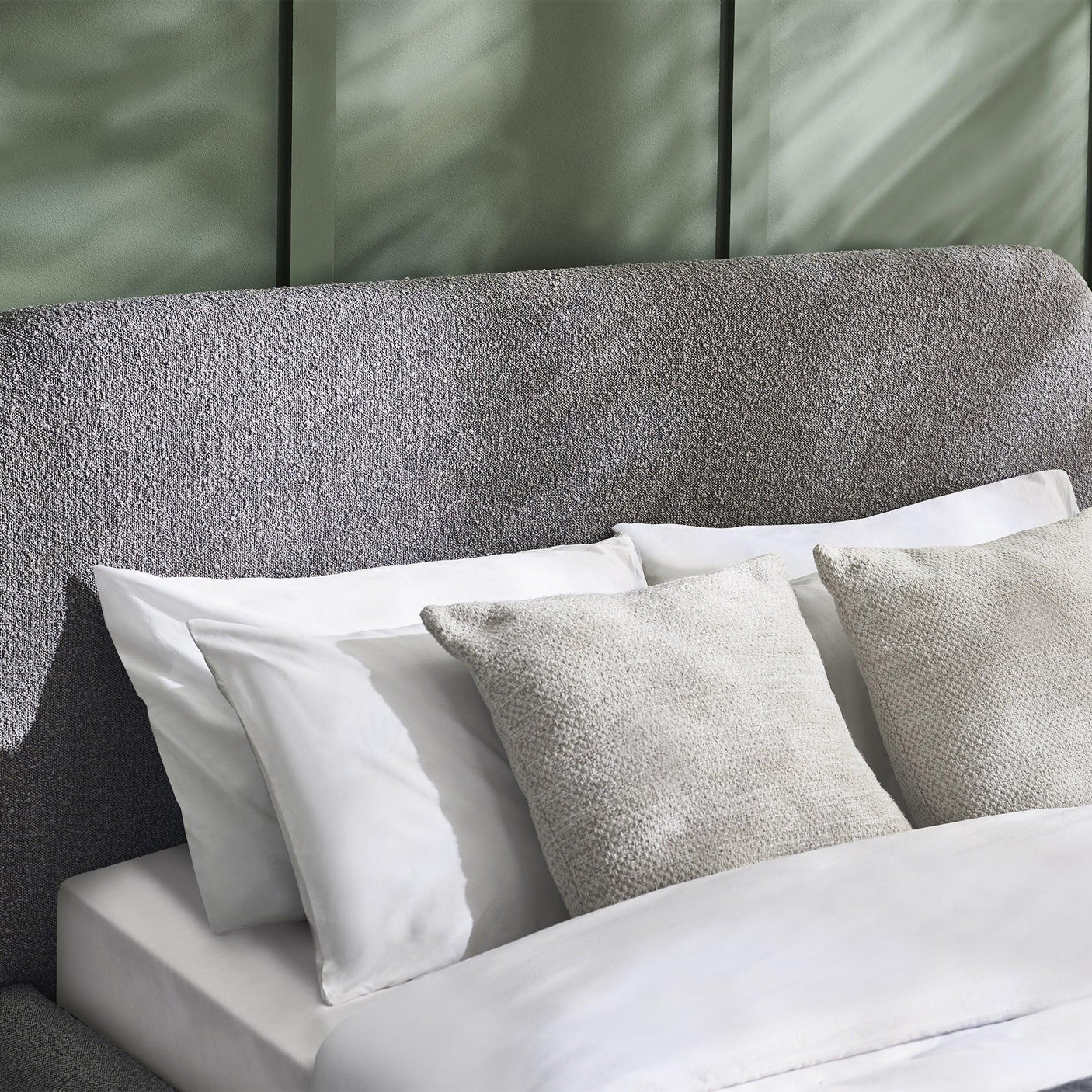 Grey upholstered bed headboard with textured fabric, white pillows and bedding