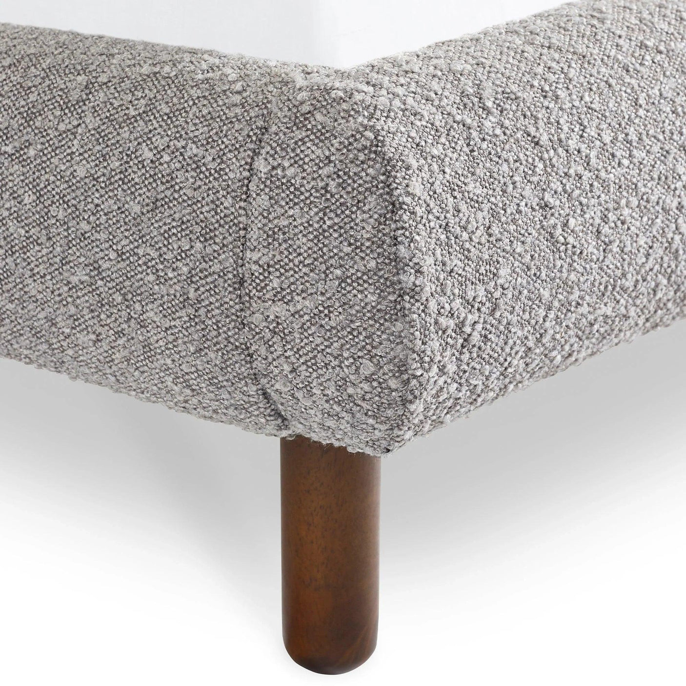 Close up of fabric bed frame corner with textured grey upholstery and wood leg