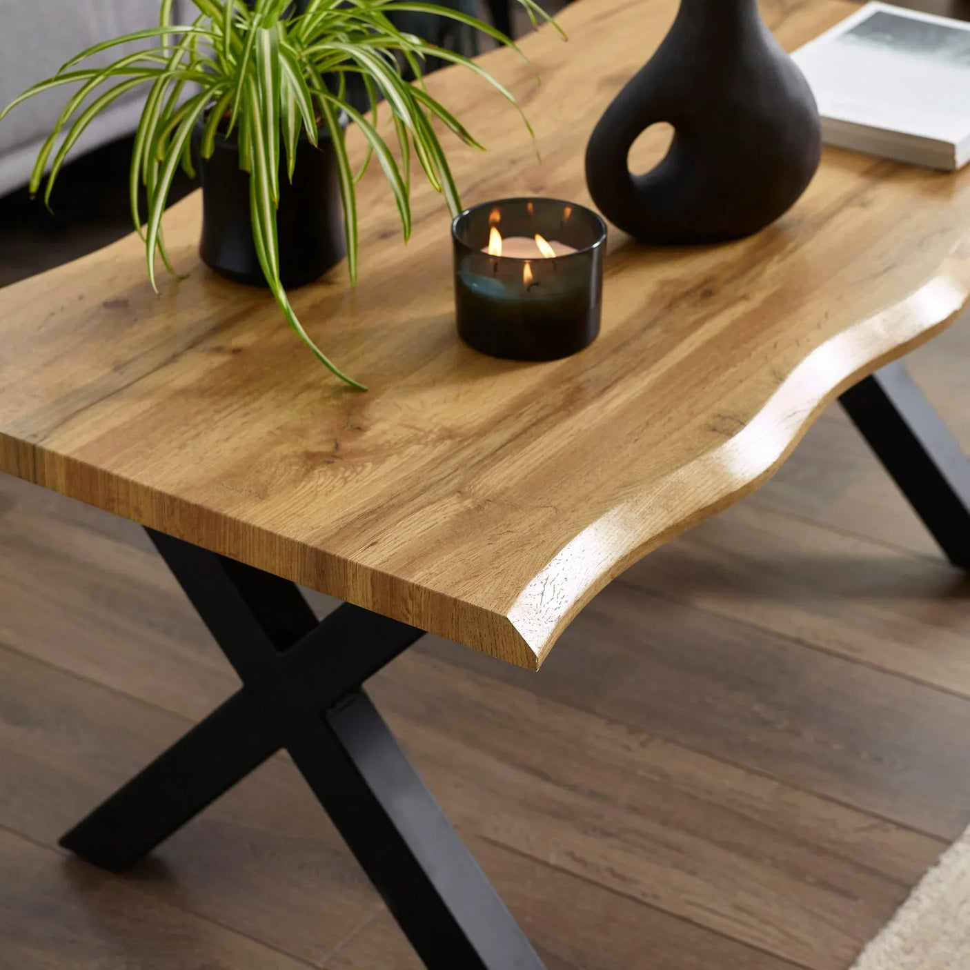 Wooden coffee table with curved edge, black metal legs, candle, and potted plant