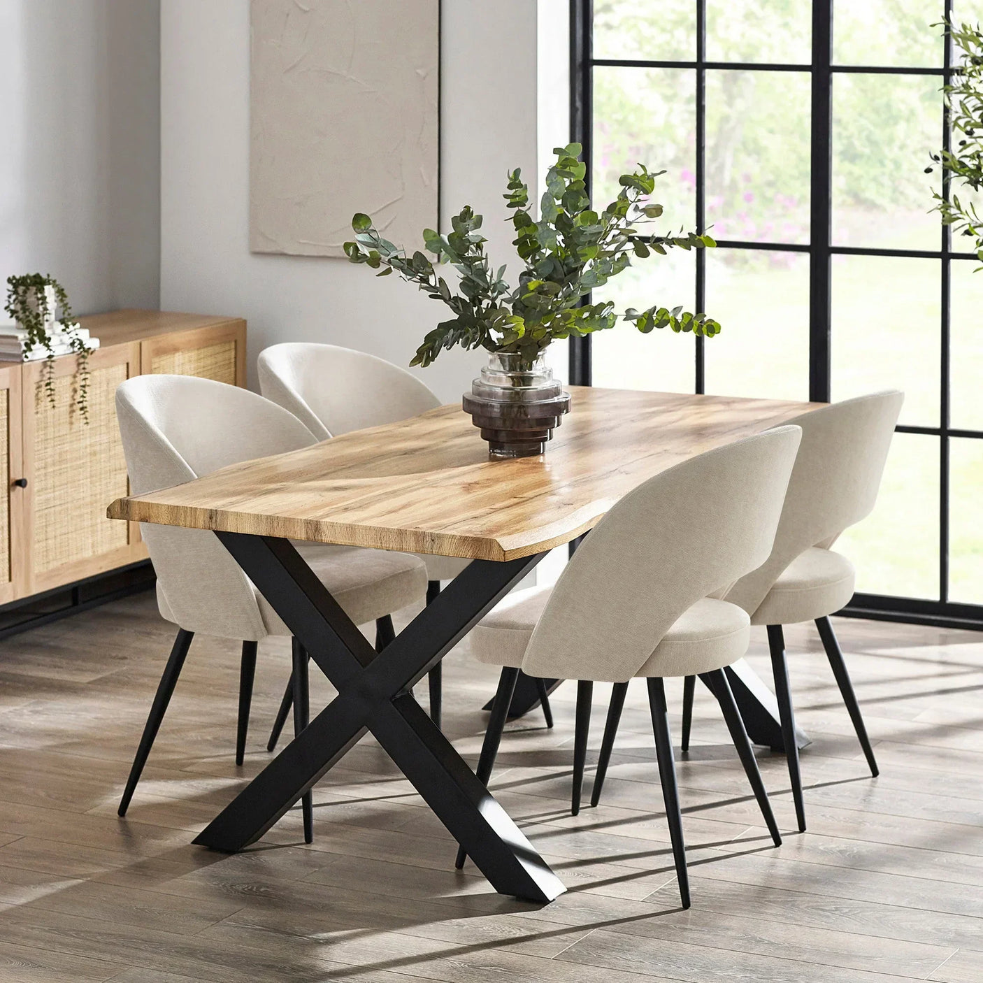Oak dining table with black metal legs and cream upholstered chairs set in a modern room