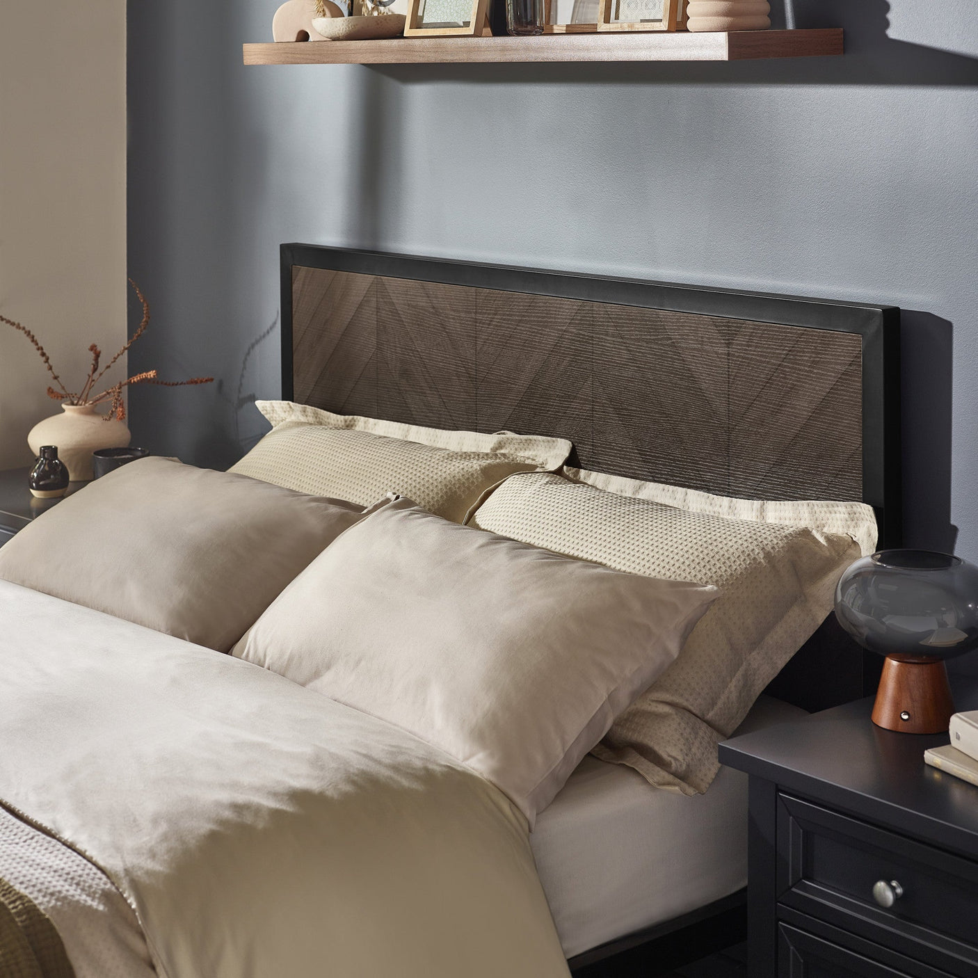 Close-up of dark wood herringbone bed footboard with cream bedding and olive throw on parquet floor
