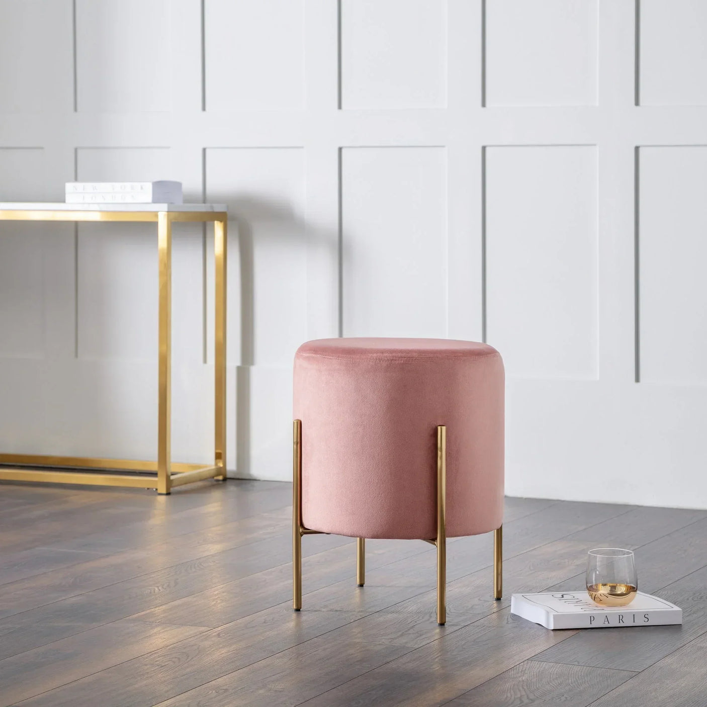 Pink velvet stool with gold legs on wooden floor beside console table and magazines