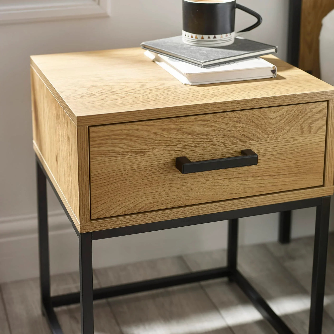 Oak bedside table with black metal legs and single drawer, books and mug on top
