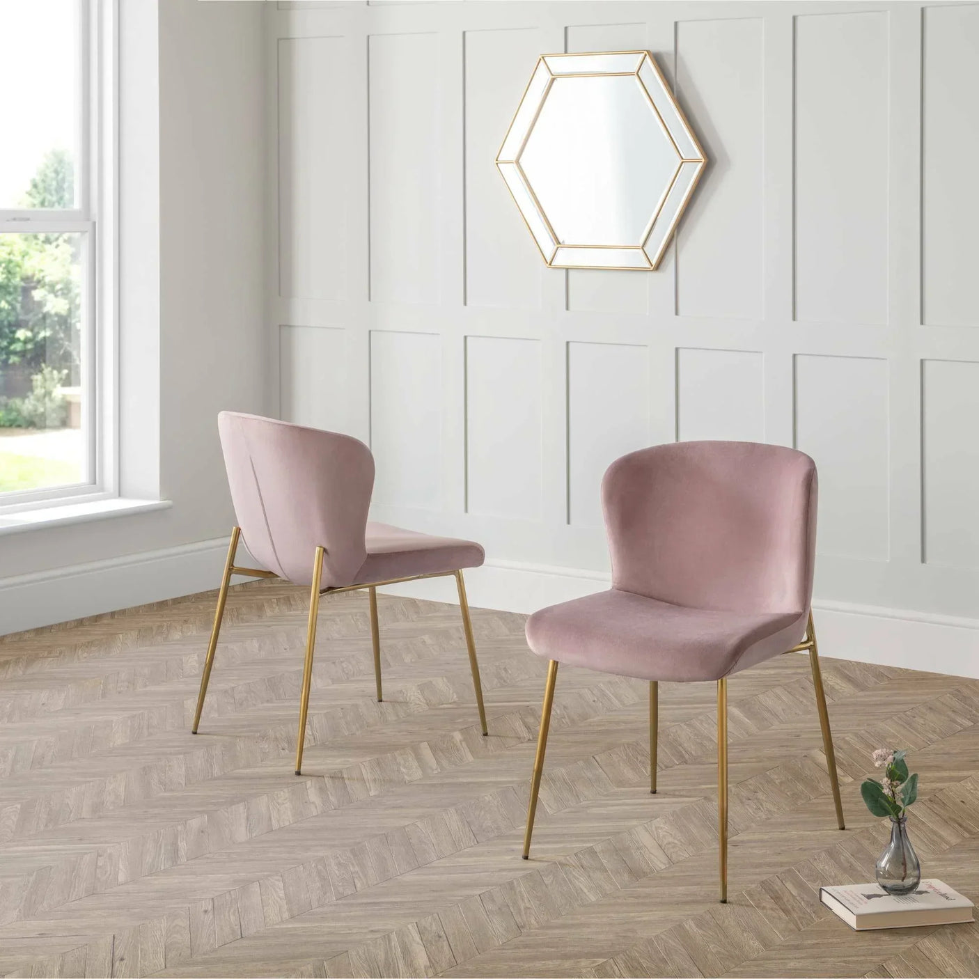 Set of two pink velvet dining chairs with gold legs in a modern room with hexagon mirror