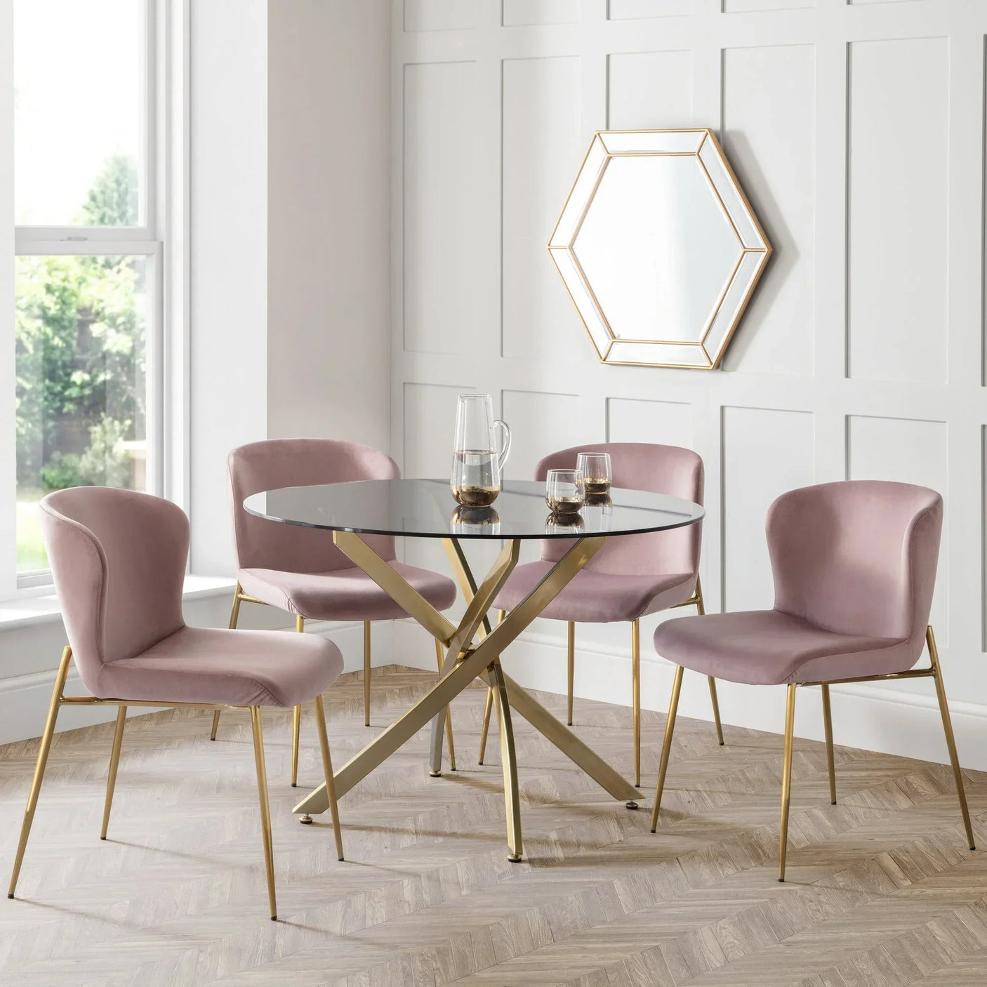 Glass dining table with gold metal legs and four pink velvet chairs in modern dining room