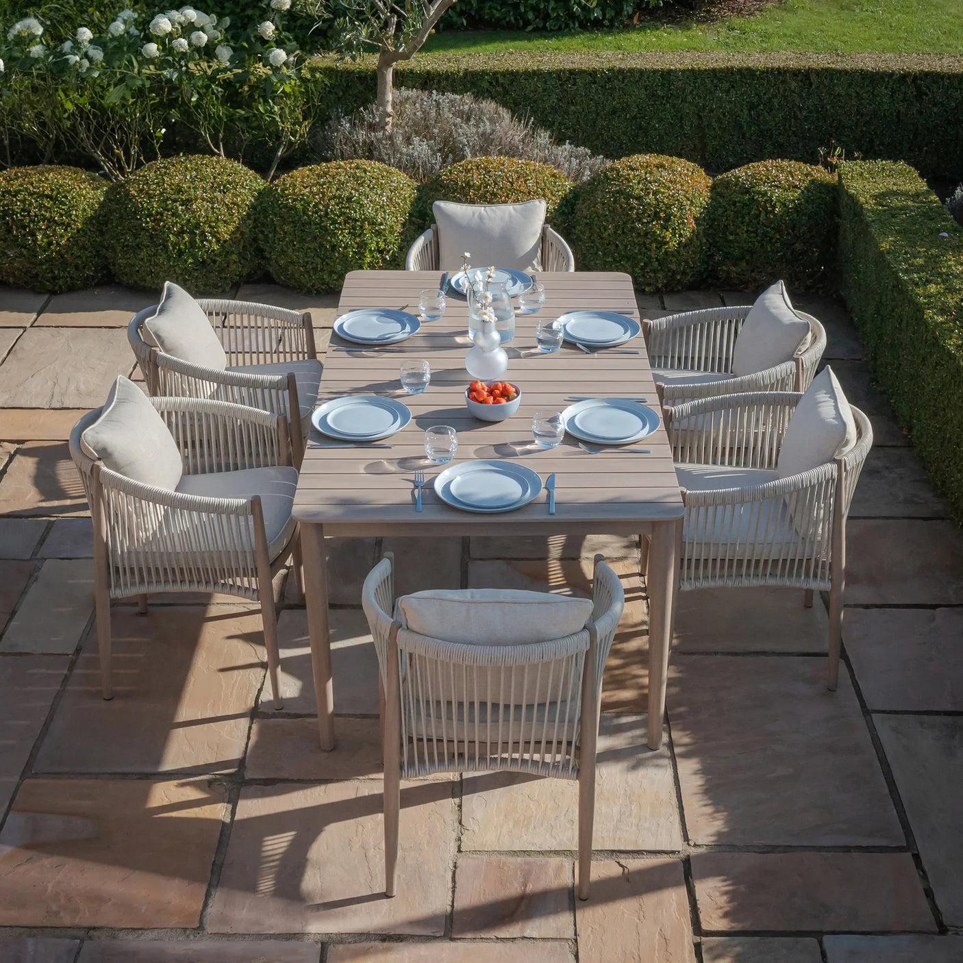 Outdoor dining set with wooden table and eight rope-back armchairs on stone patio