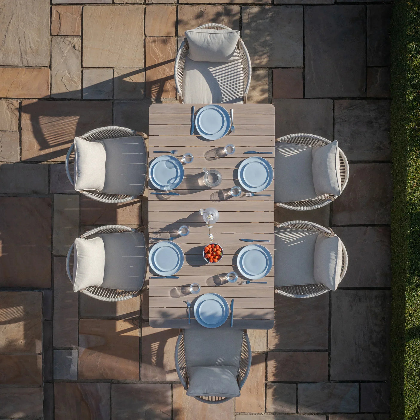 Rectangular outdoor dining set with six cushioned chairs on stone patio, set for a meal