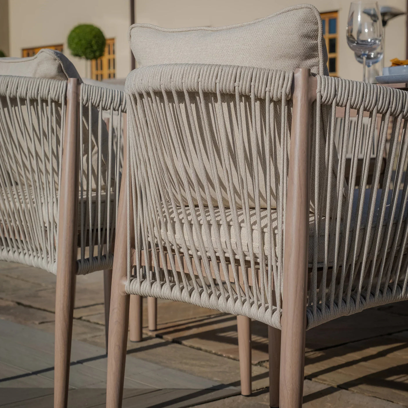 Beige rope outdoor dining chairs with cushioned seats on a stone patio