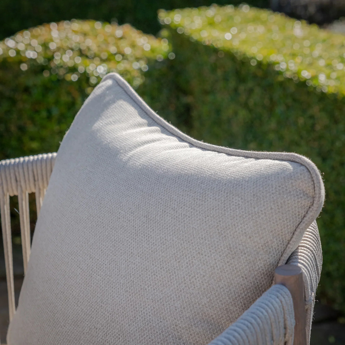 Outdoor sofa with beige textured cushion and rope detail armrest in garden setting