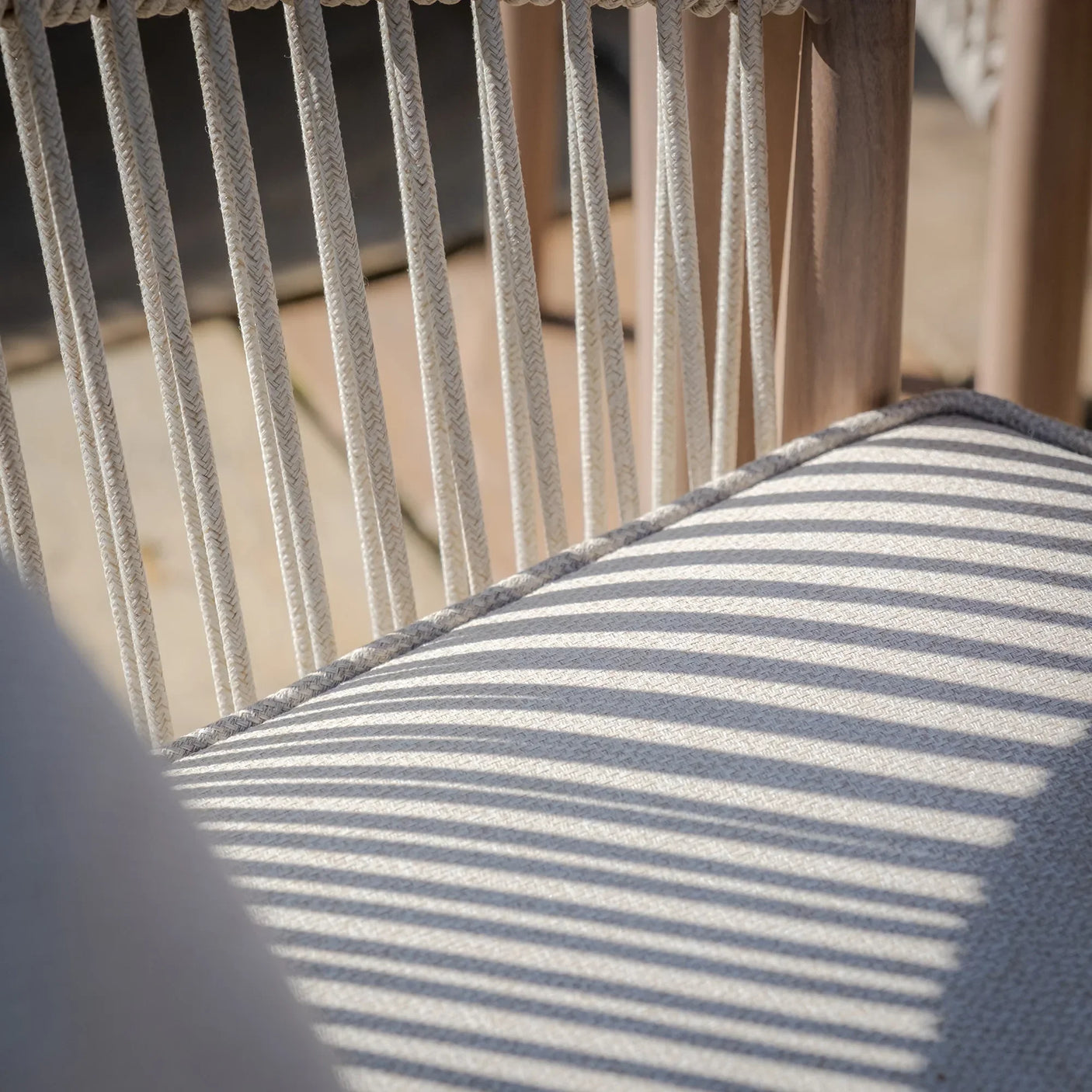Closeup of beige rope-back outdoor chair with cushioned seat in sunlight