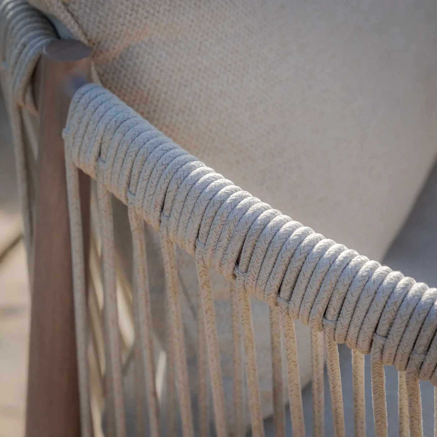Closeup of cream rope detail on wooden outdoor chair with textured fabric cushion