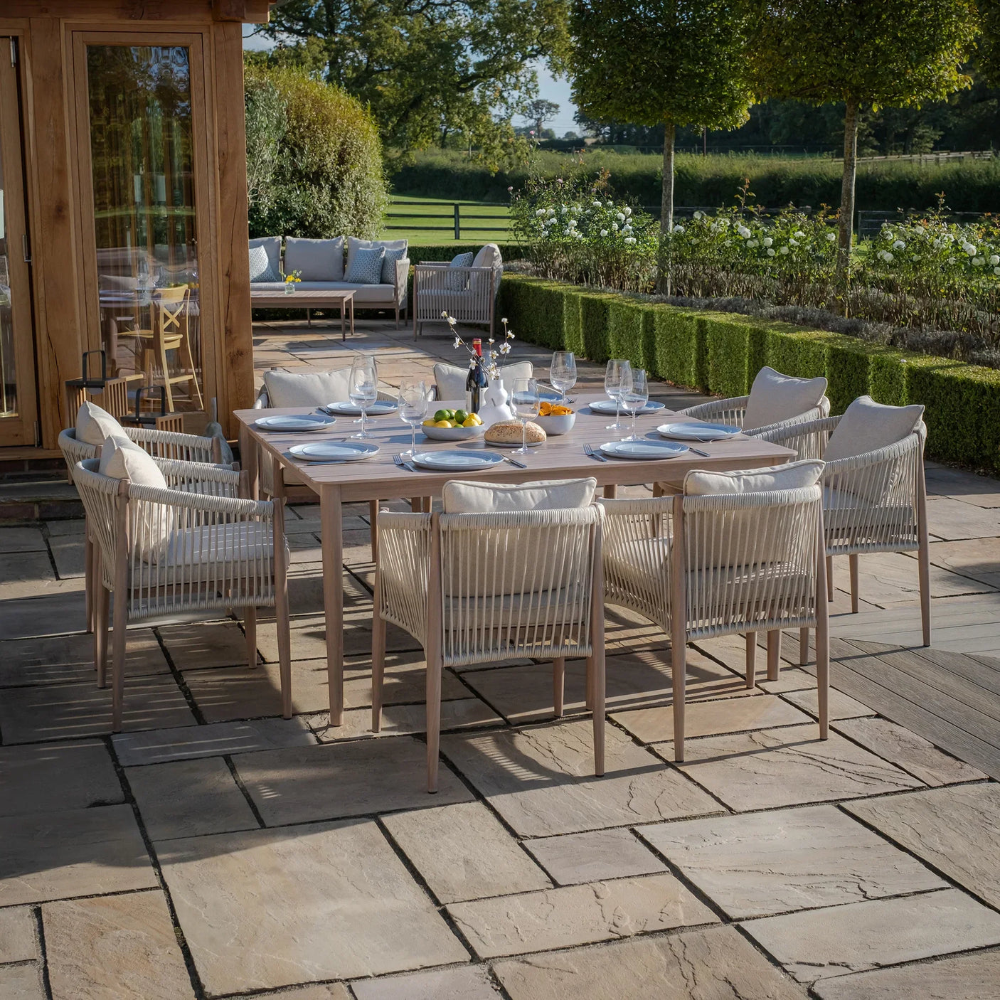 Outdoor dining table set with rope chairs and neutral cushions on stone patio
