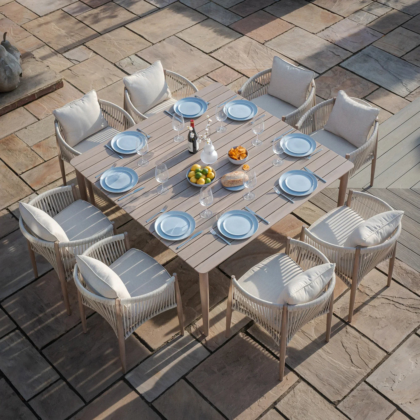 Outdoor dining set with rope chairs, wood table, and tableware on stone patio