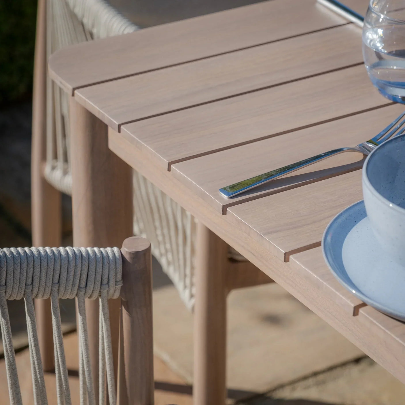Light wood outdoor dining table with slatted top and rope detail chairs, close up