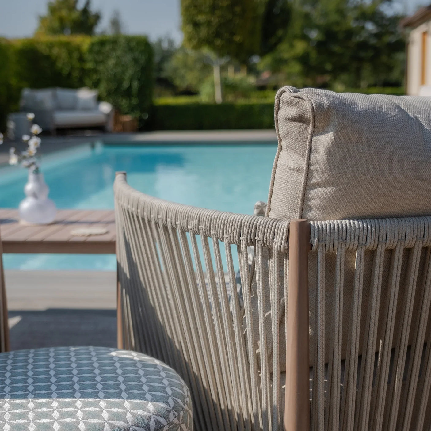 Beige rope outdoor sofa with cushion by pool and patterned round ottoman