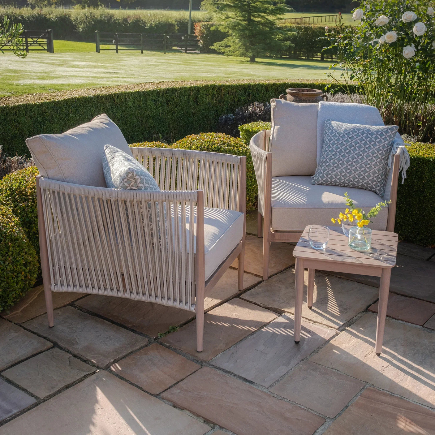 Beige rope outdoor lounge chairs with cushions and side table on stone patio
