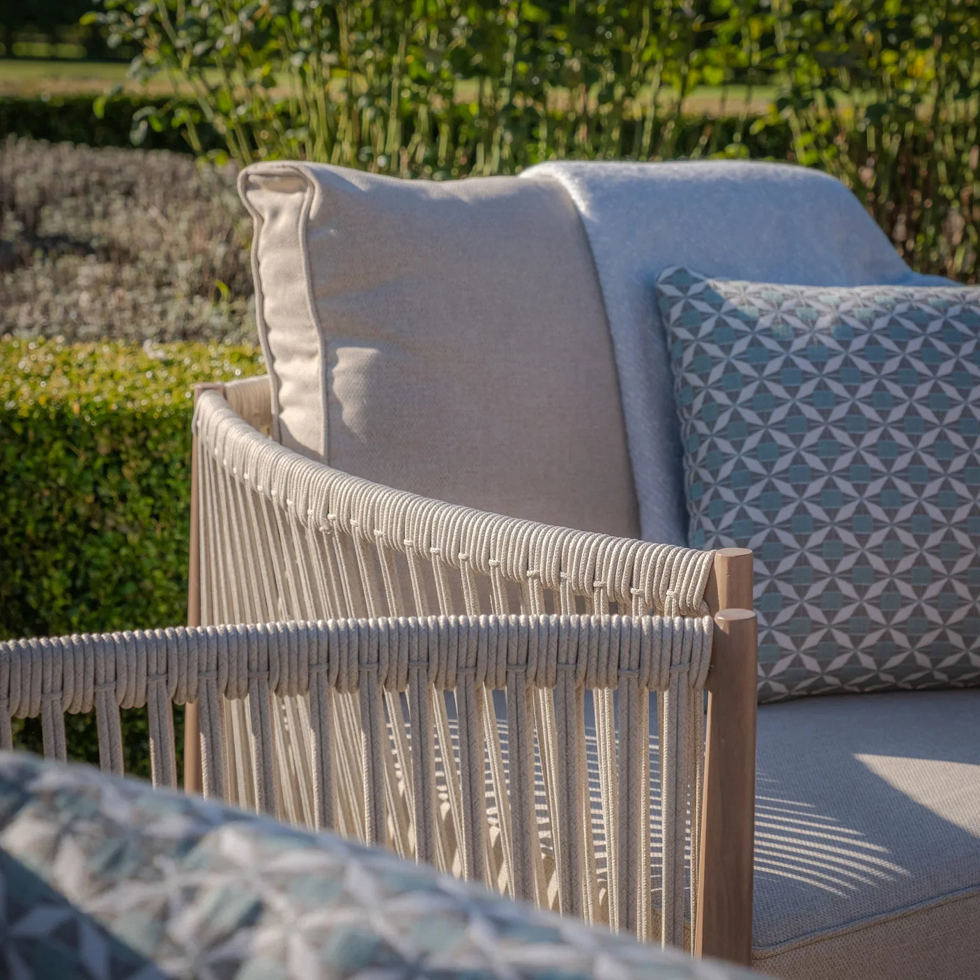 Beige rope outdoor sofa with geometric patterned cushion and garden background