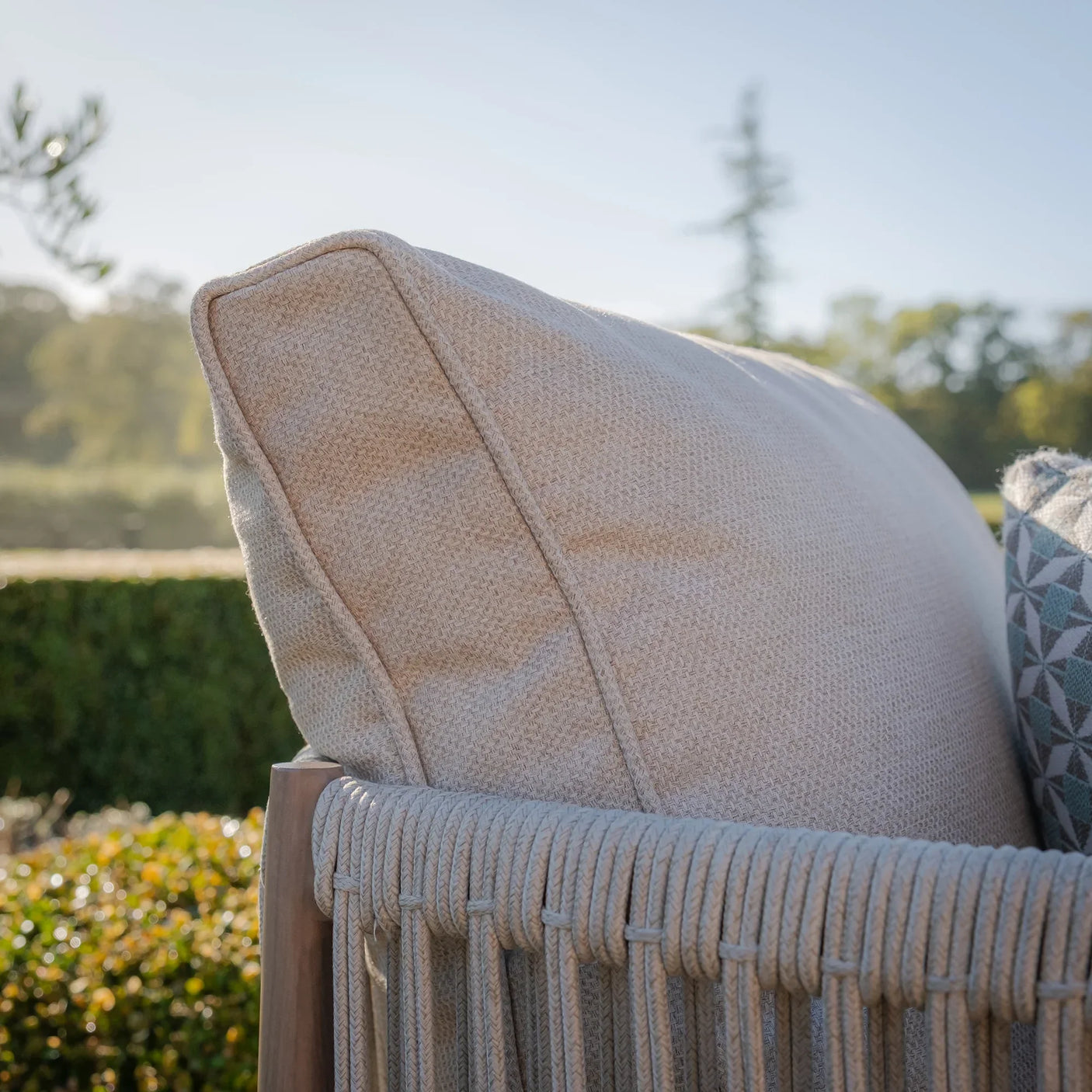 Beige outdoor sofa cushion with woven rope armrest in garden setting