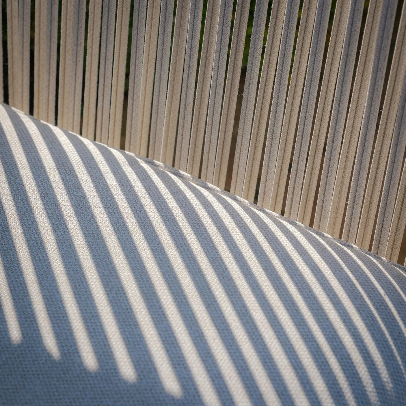Close-up of beige rope backrest and cushion on outdoor lounge chair with sunlight shadows