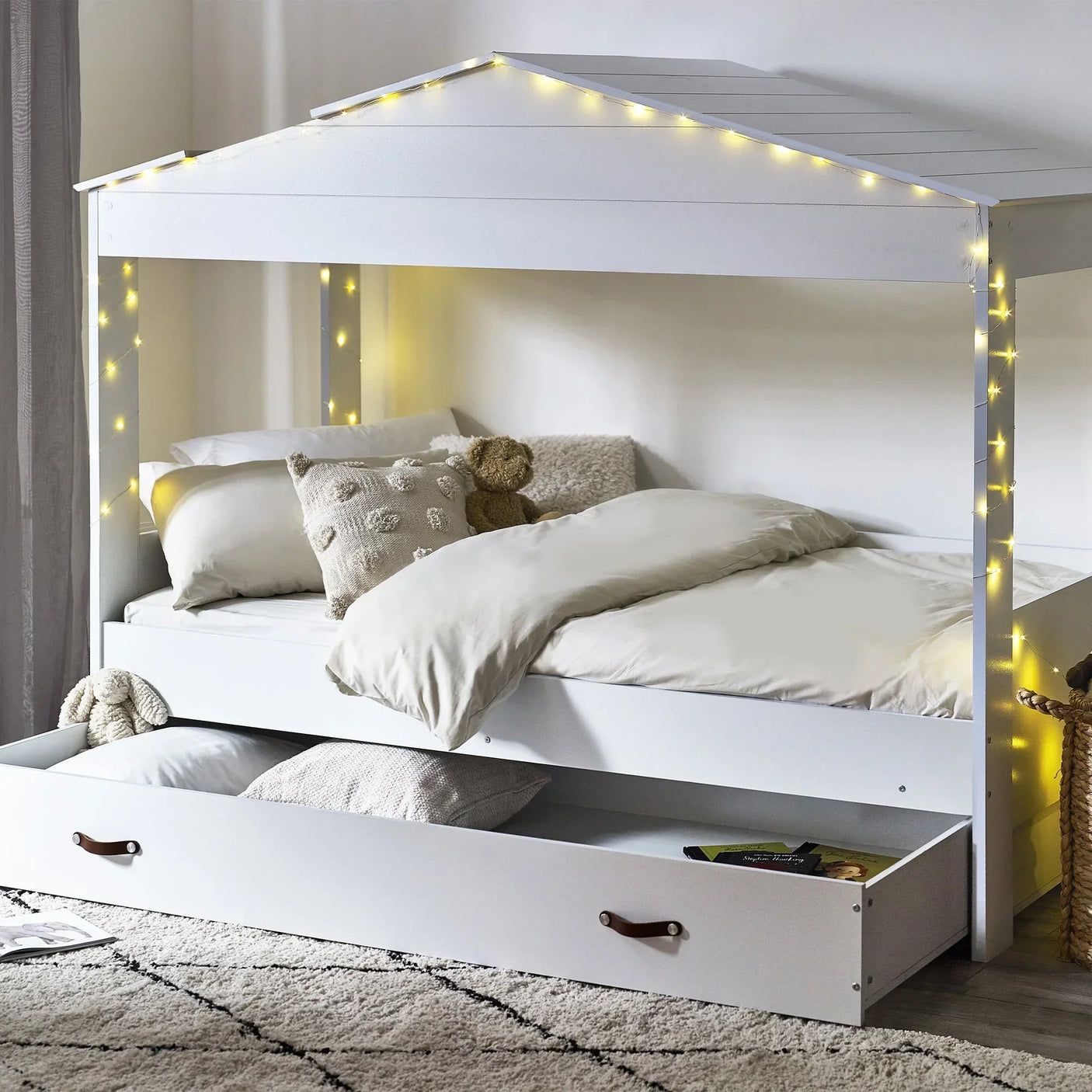 White kids low sleeper bed with roof frame, string lights, storage drawer, and bedding