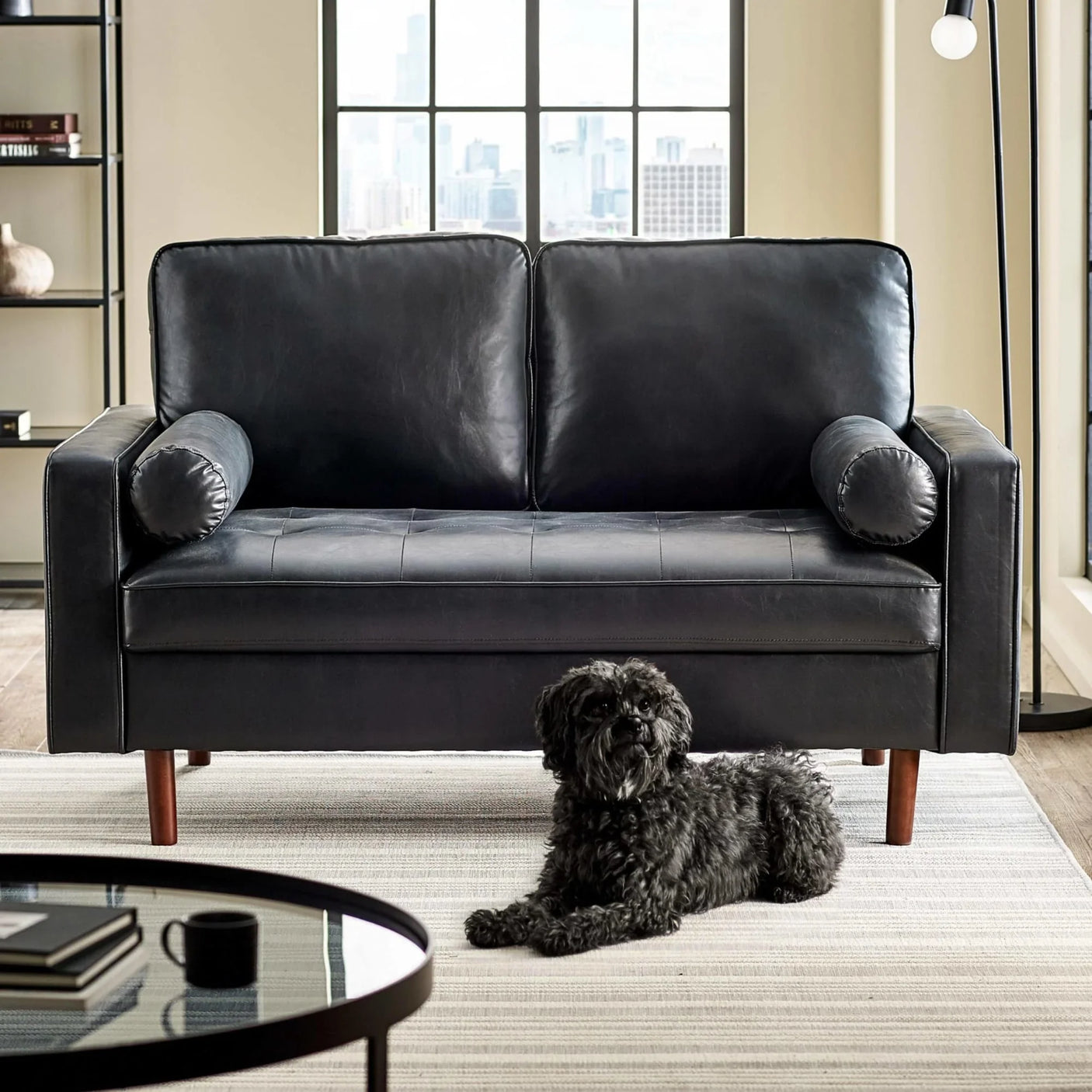 Black leather sofa with round bolster cushions in modern living room, dog on striped rug
