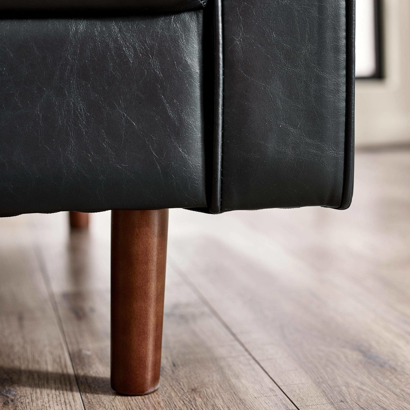 Black leather sofa corner with slim wooden leg on light wood floor