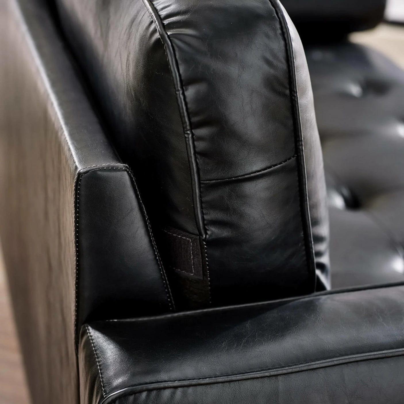 Close view of black leather sofa cushion and stitched armrest
