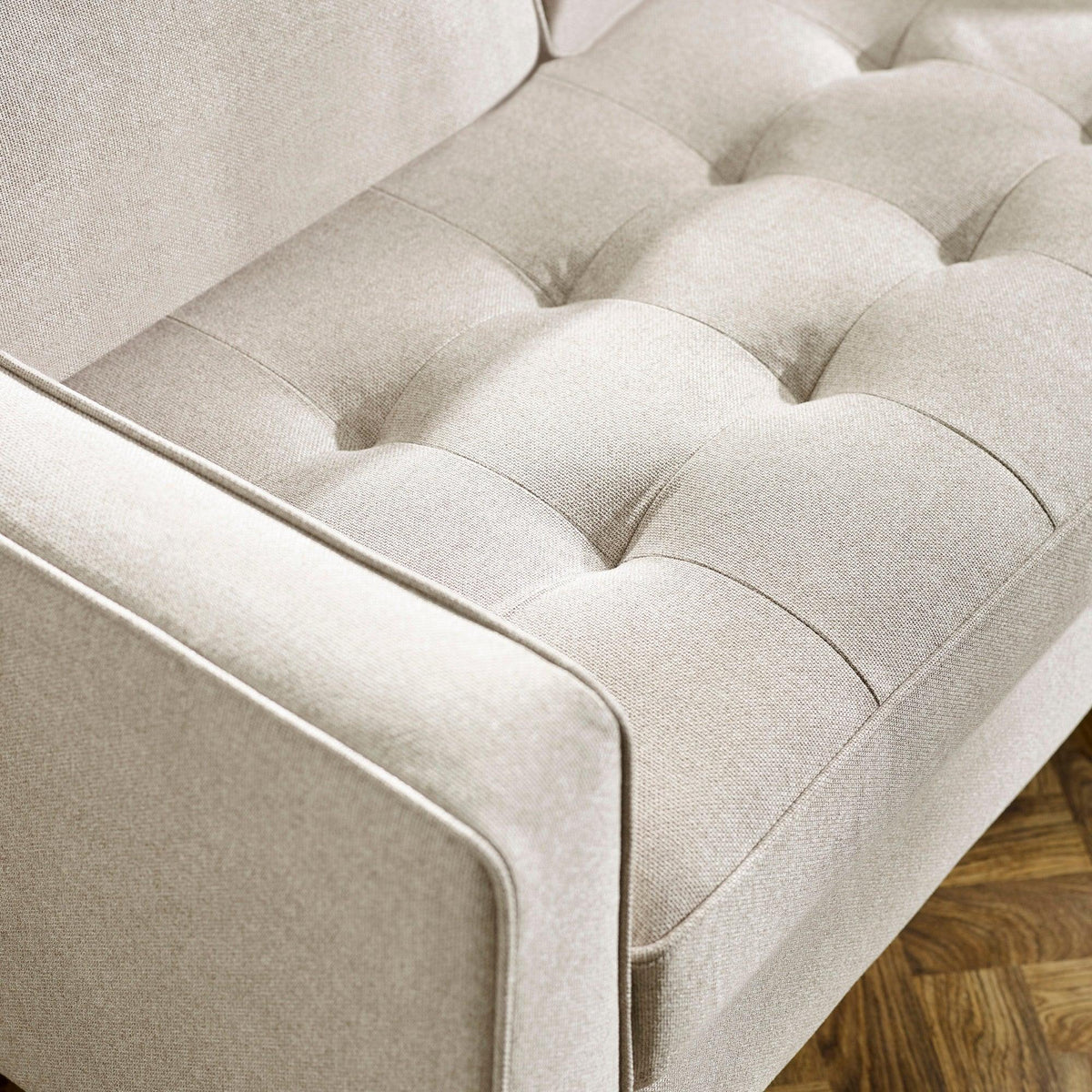 Beige fabric sofa with tufted seat cushion and armrest, close-up on wood floor