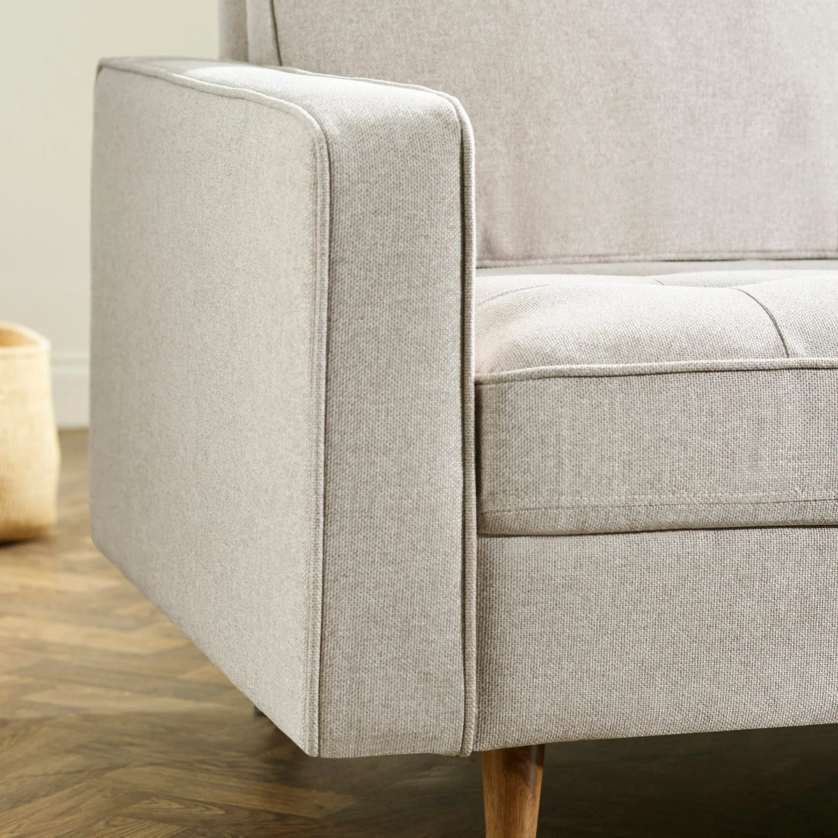 Beige fabric sofa arm with wooden leg and textured upholstery detail on hardwood floor