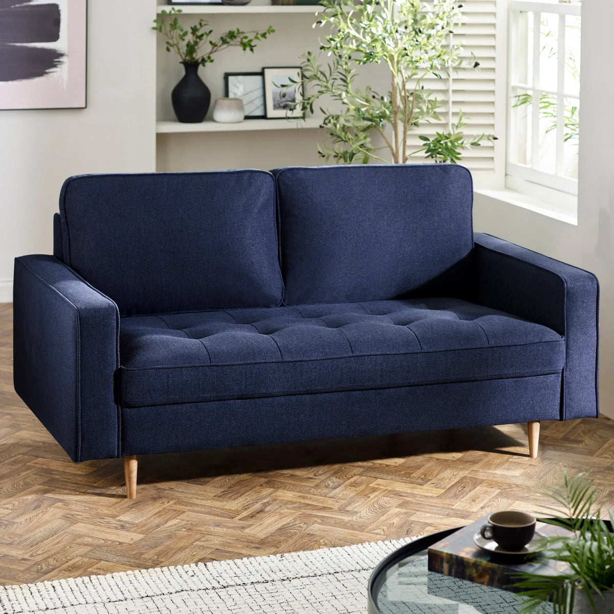 Navy blue fabric sofa with wooden legs in modern living room setting near window