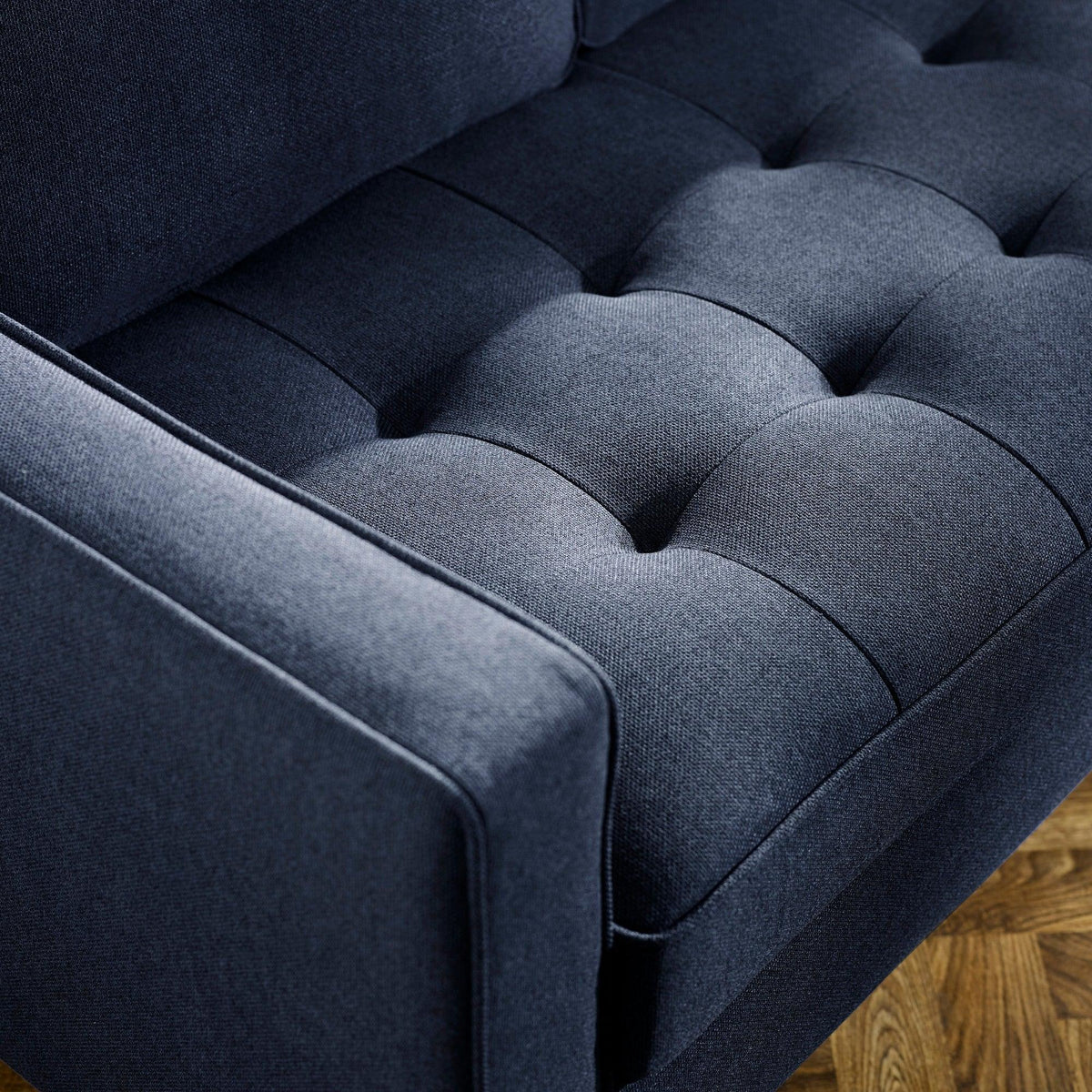 Dark blue fabric sofa with deep buttoned seat detail and angled armrest