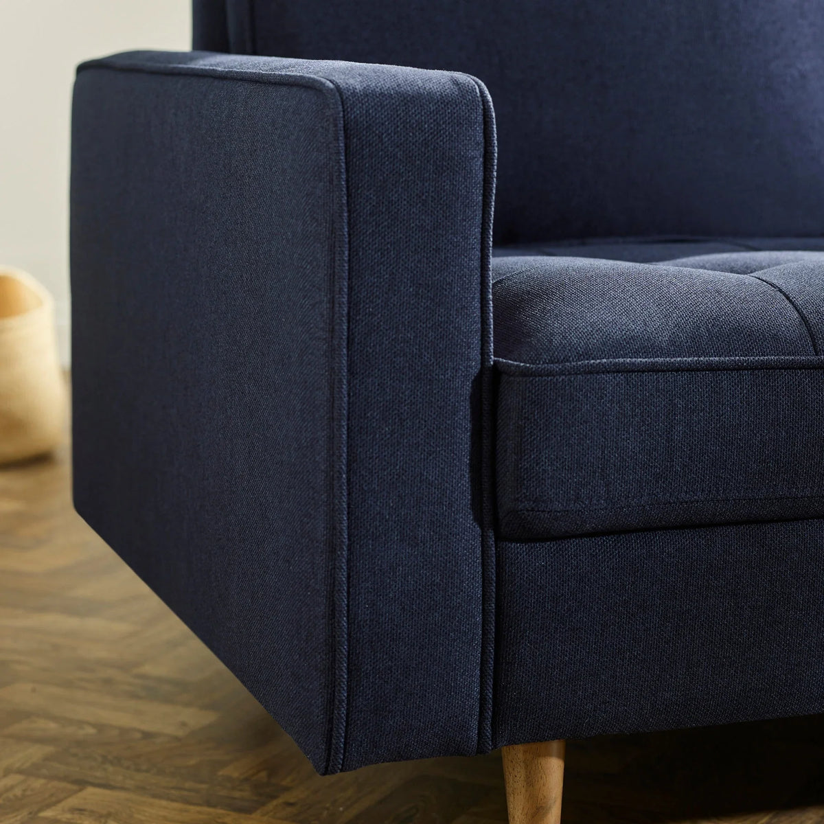 Close-up of navy fabric sofa armrest with wooden leg on herringbone floor